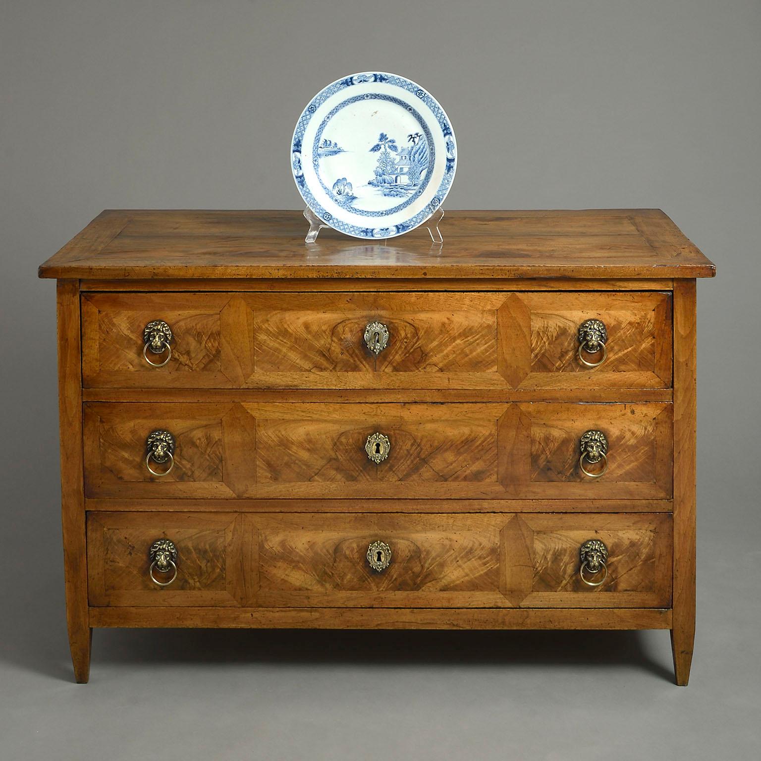 A fine late 18th century walnut commode of good soft color in the neoclassical manner, the overhanging top above three finely figured panel veneered drawers, with brass lion mask handles and lock escutcheons, all raised on square tapering feet.
