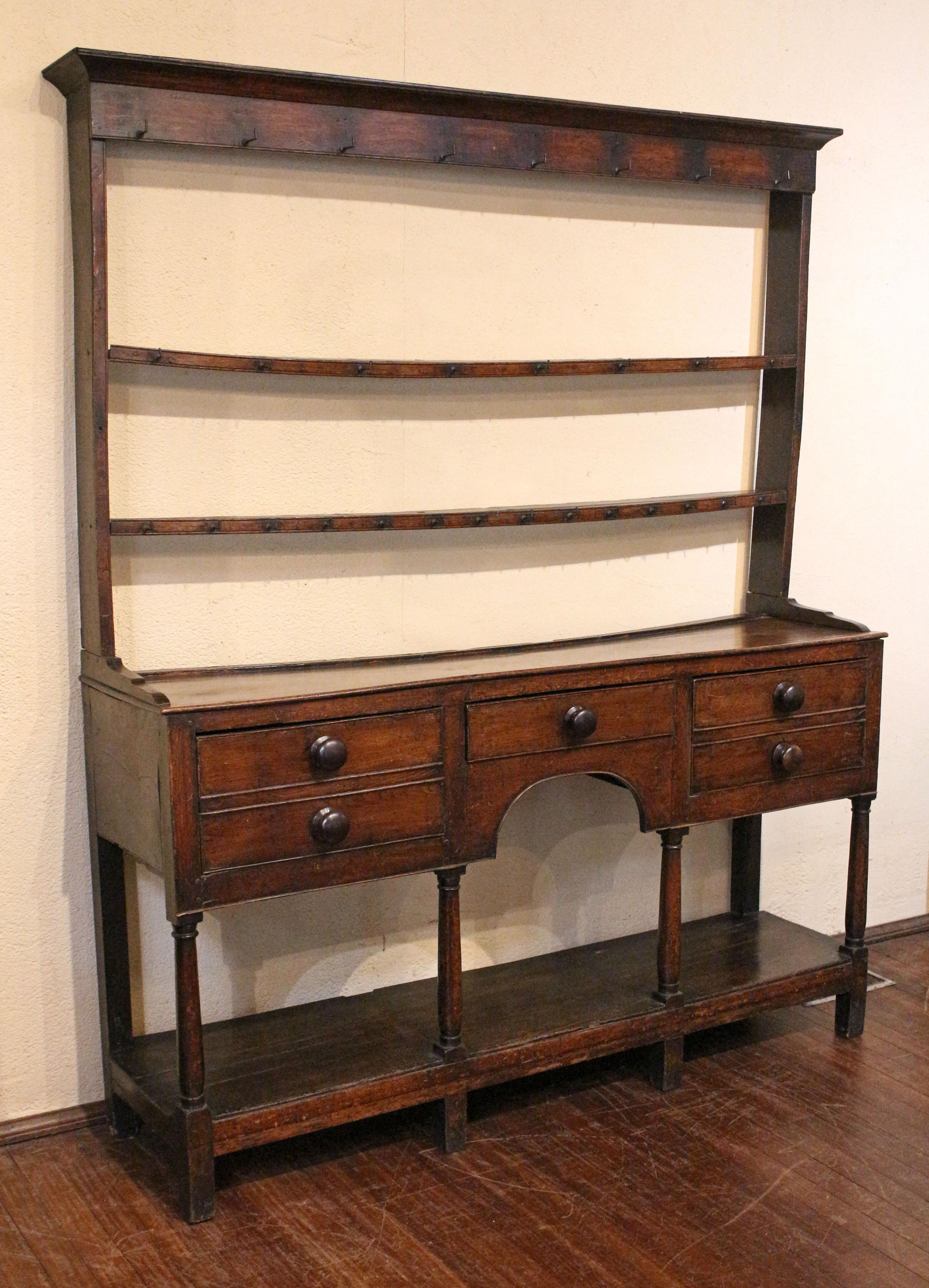 Late 18th century Welsh Dresser with pot shelf base, Wales. Elm & ash. The handsome columns are simply swell turned. Deep drawers, with double drawer faux fronts for visual design continuity, flank a single drawer over arched opening. Forged iron