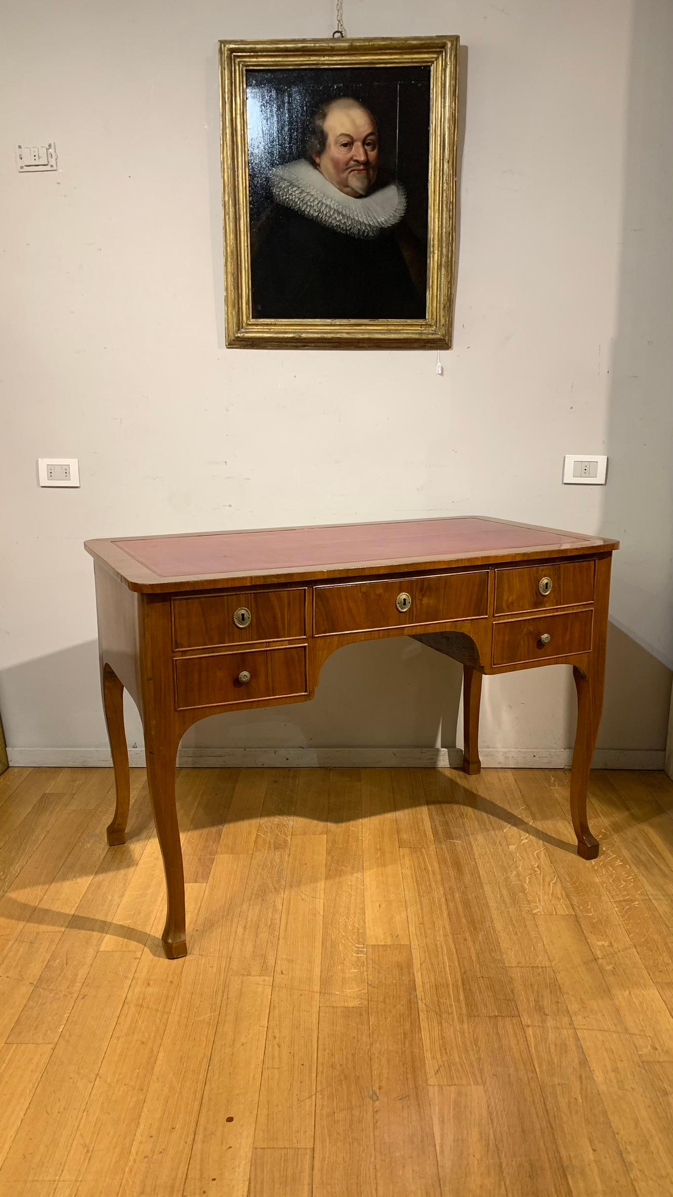 Beautiful writing table veneered in walnut with top partially covered in red-purple leather and highlighted in gold.
Five drawers, four of which are smaller on the sides and one in the centre, wavy legs.
Tuscan manufacture from the end of the