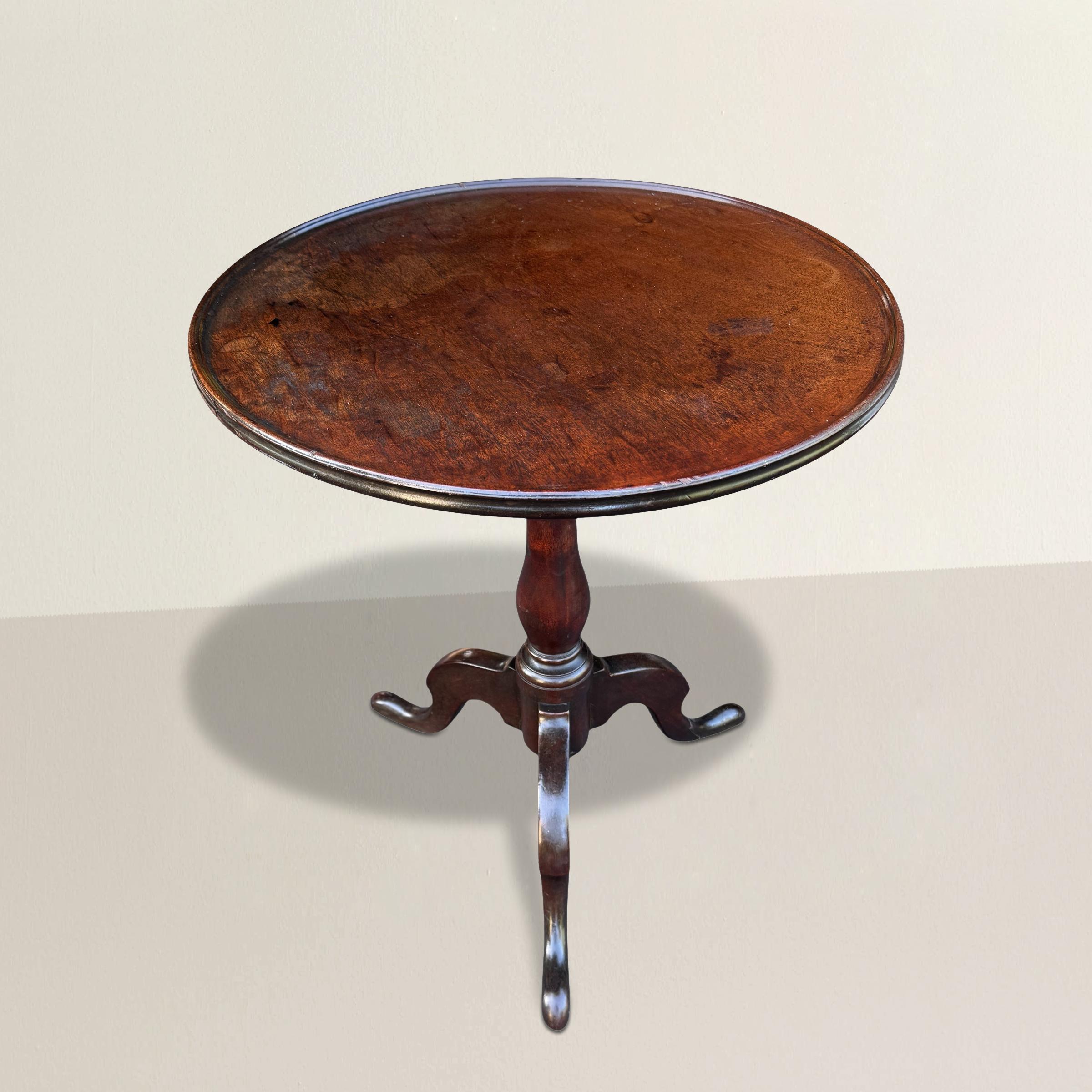 This late 18th/early 19th century American tilt-top table is a graceful survivor of early American furniture, crafted from solid mahogany with a round top made from a single board—an increasingly rare and telling sign of age and quality. The top is