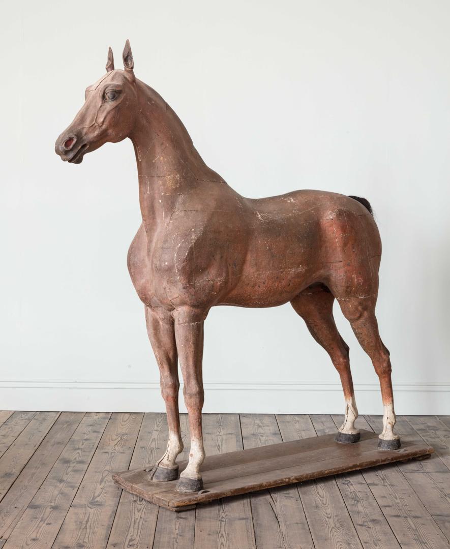 A late 18th-early 19th century full size wooden sculpture of a horse, with tail made from horse hair, resting on a rectangular wooden base mounted on four castors.