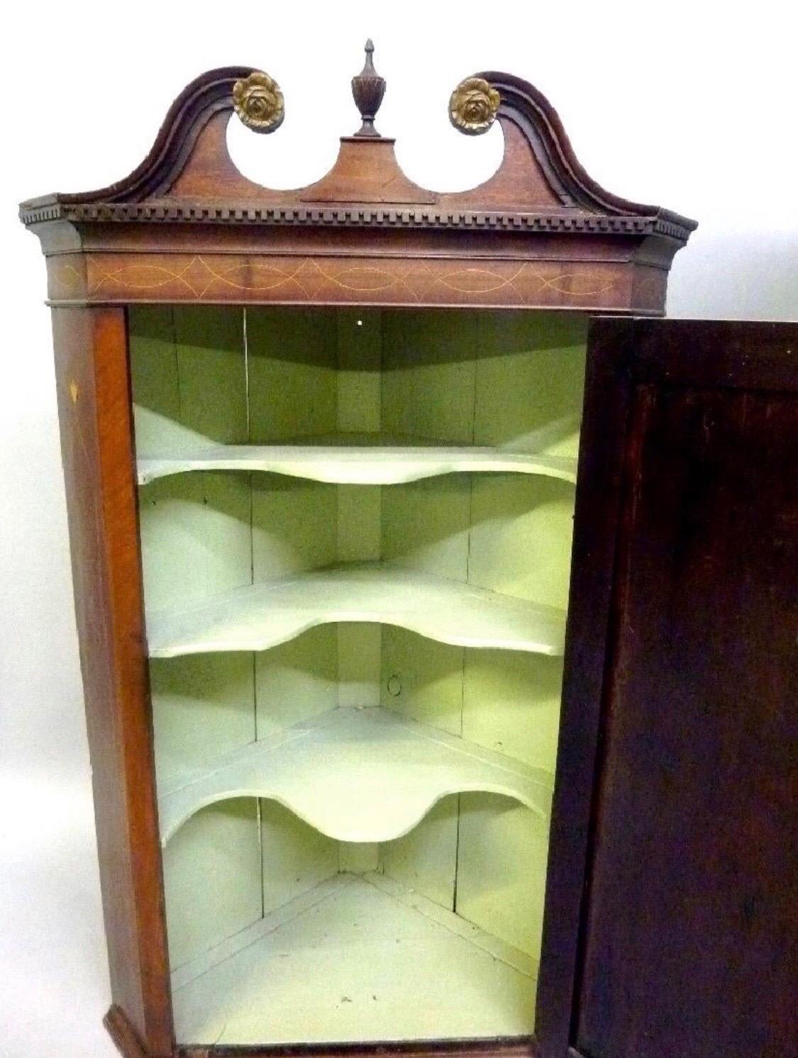 Late 18th-early 19th century Georgian mahogany inlaid hanging corner cabinet with single door, inlay banding and broken pediment cresting with finial. Has great green interior with scalloped shelves inside.
 