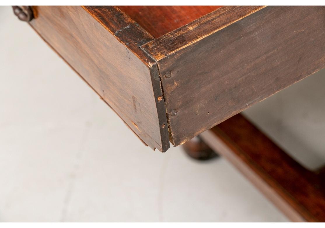 A fine late 18th-early 19th century tavern/work table with strongly turned legs, ball feet, breadboard plank top and bottom H-form stretcher. The table has a long drawer on one end with a ring pull and stylized flower escutcheon. The table has a