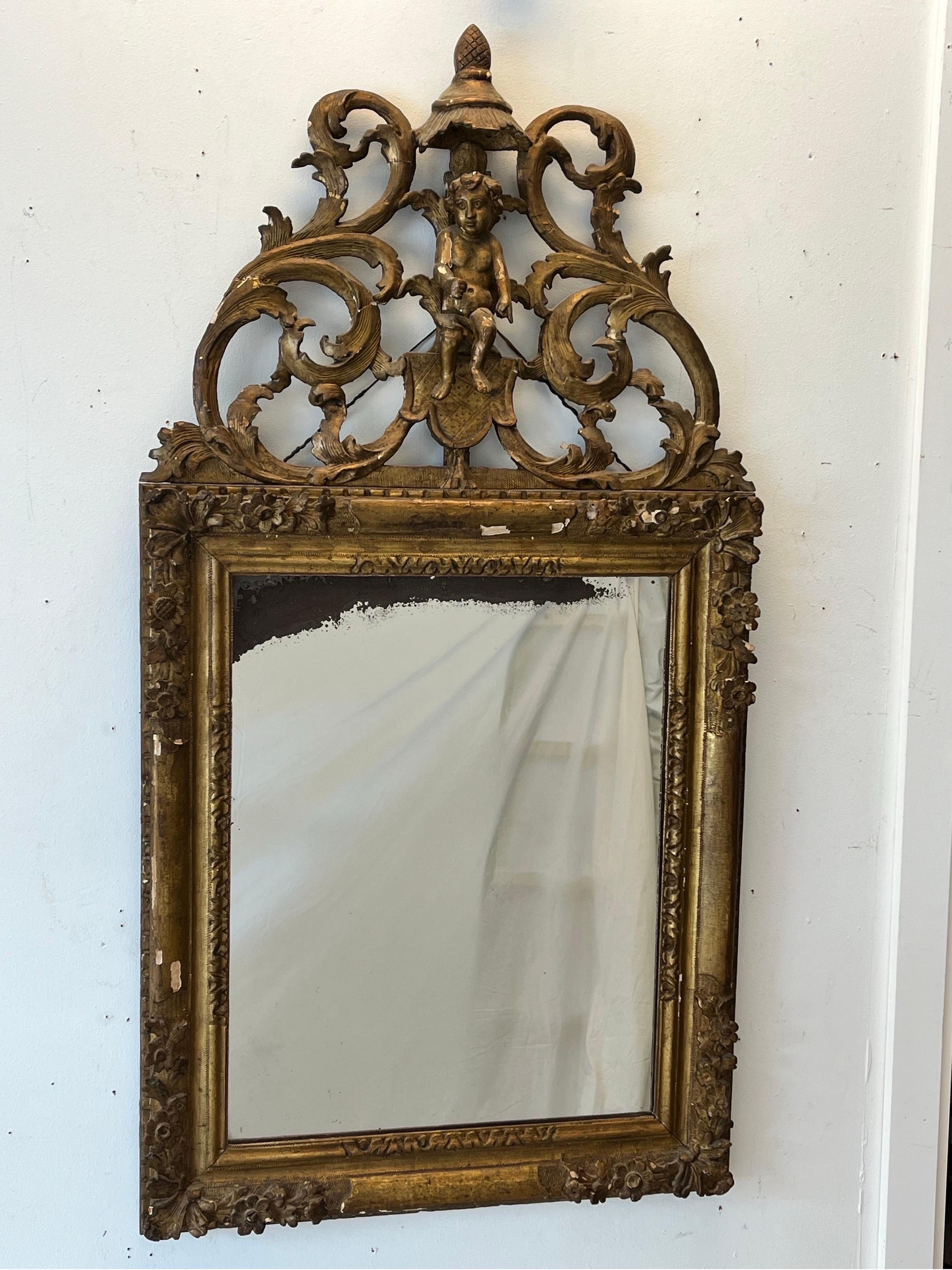 An incredible and unique antique Louis XIII / XIV Regence style late 18th / early 19th Century hand carved and gold leafed frame with an ornately designed cornice piece featuring a fully carved cherub or putti. The scrolling and ornately carved top