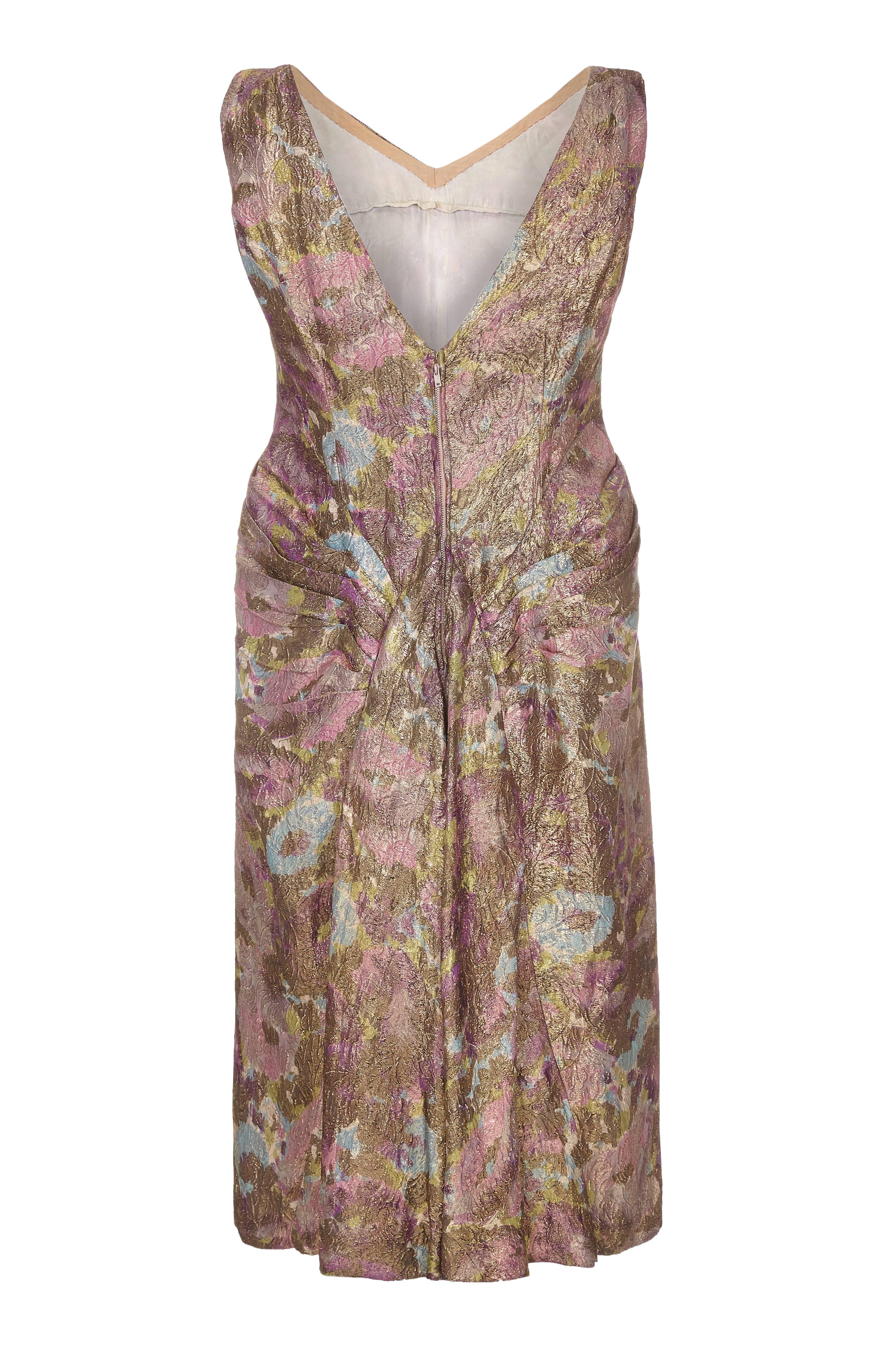 This irresistibly pretty late 1950's lame cocktail dress is lovely in both its delicate surface texture and its cleverly constructed design. The fabric is slightly embossed with a subtle leaf motif, accentuated by fine gold thread running through