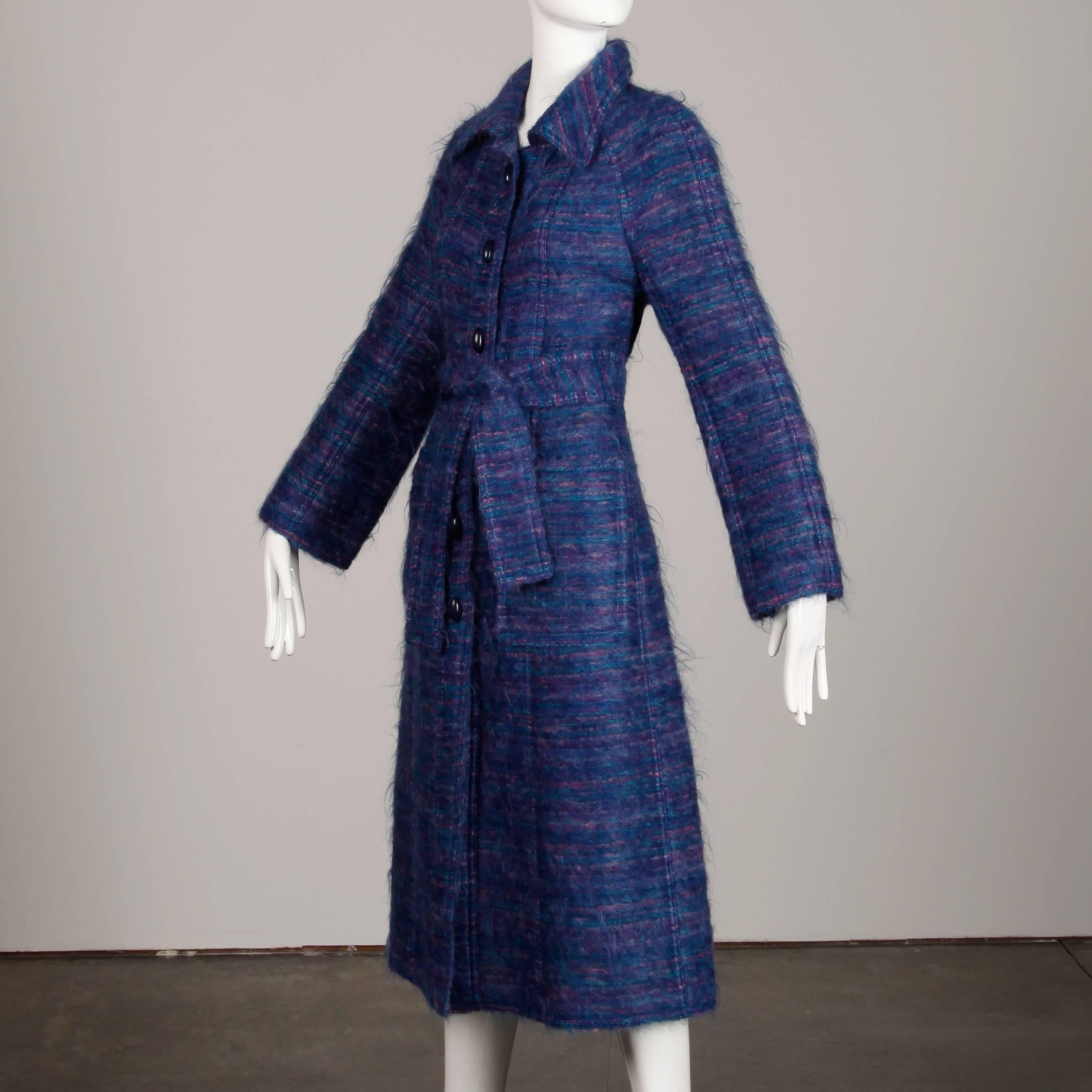 Magnifique manteau vintage de Bernard Perris en mohair tissé violet et bleu, avec ceinture cravate assortie. Partiellement doublé, il se ferme par un bouton et une cravate sur le devant. Poches latérales plaquées. Le buste mesure 38