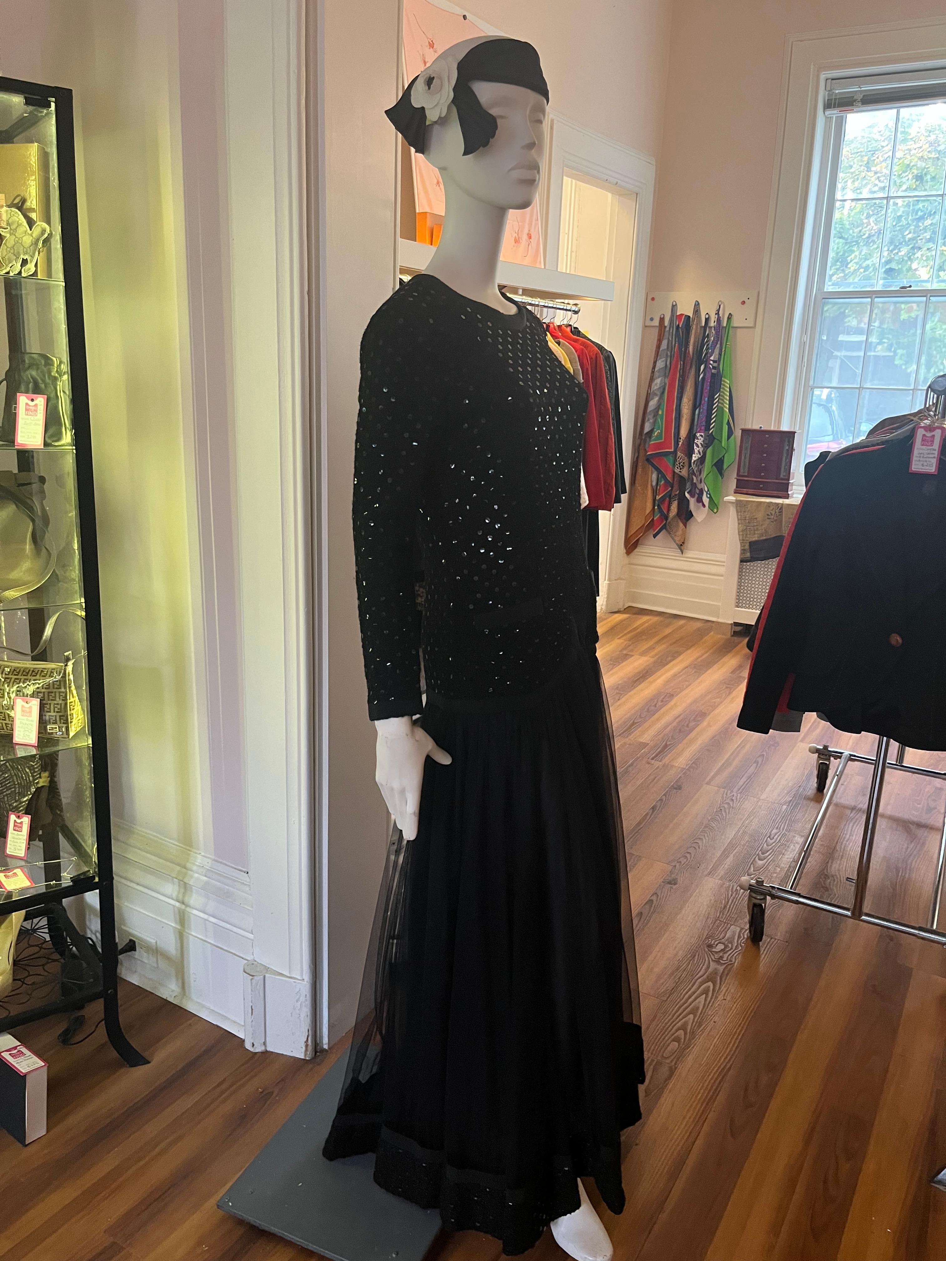 This is a very special full-length gown with a drop waist ending in a grosgrain trimmed inverted v. 

The  sequin/boucle top and long sleeves  also have a grosgrain trim which is replicated at the hem . As part of the drop waist there are also two
