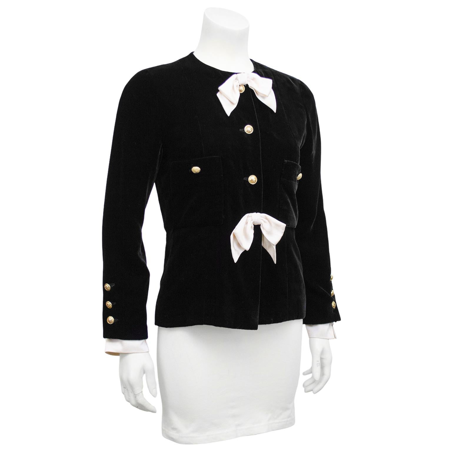 Stunning and classic fitted Chanel collarless jacket from the late 1980's. Jet black silk velvet with cream satin bow details at collar and waist, and cream satin removable cuffs. Gold tone buttons with filagree flower details. Patch pockets at bust