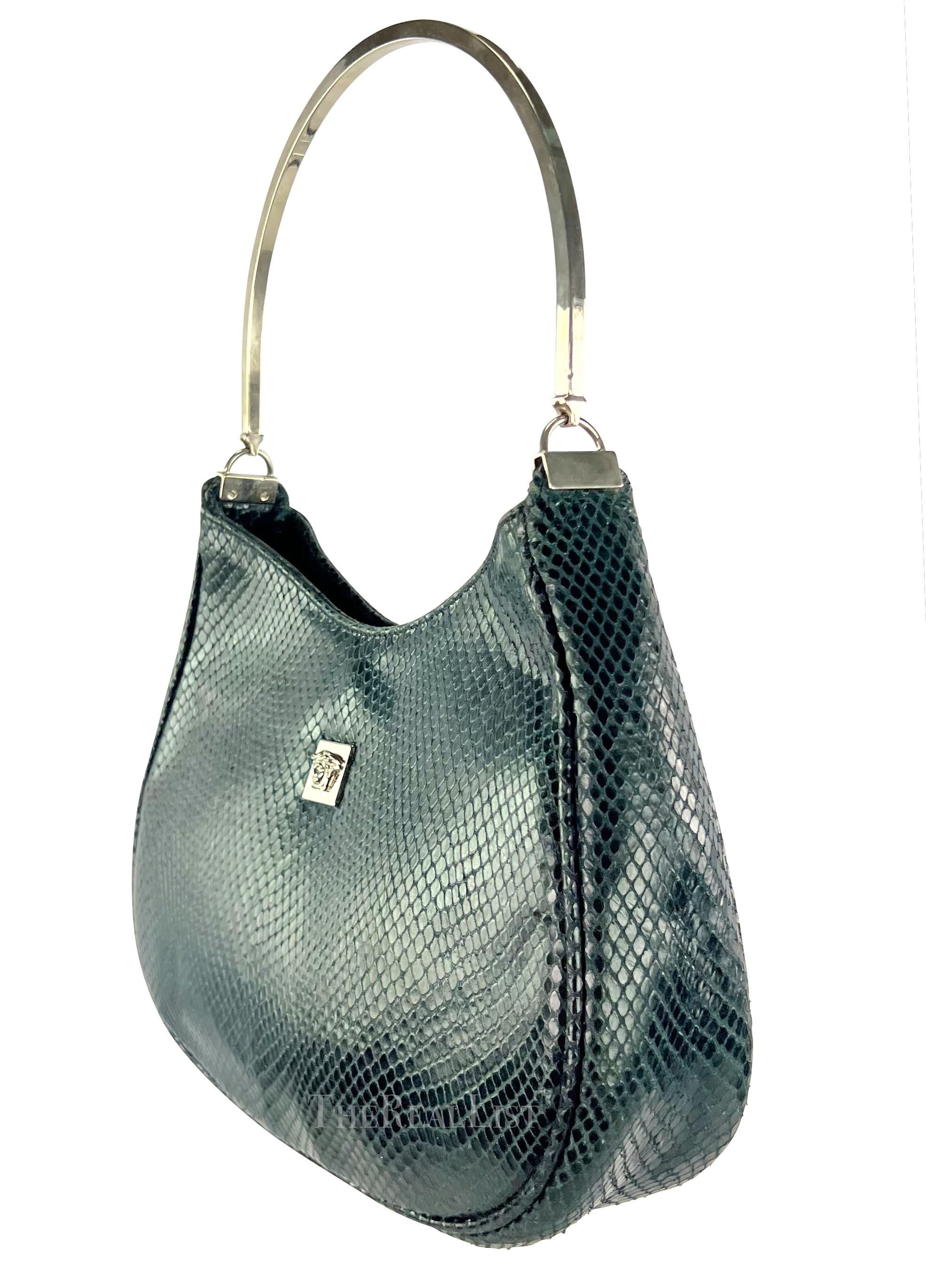 Ti presentiamo uno splendido Gianni Versace in pelle di serpente color verde acqua. Questa borsa degli anni '90 presenta una squisita struttura in pelle di serpente color verde acqua. Il suo manico rotondo in metallo argentato e l'accattivante