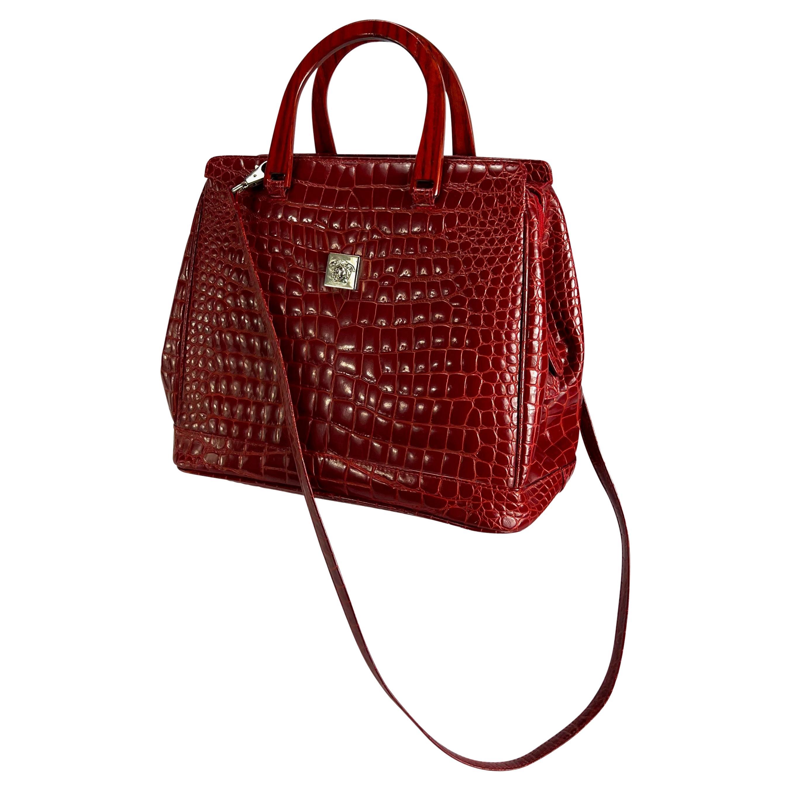 Ti presentiamo una favolosa borsa con manico superiore in coccodrillo rosso brillante disegnata da Gianni Designs. Questa borsa presenta manici superiori in legno rosso e una tracolla più lunga rimovibile. È completata da una targhetta Medusa