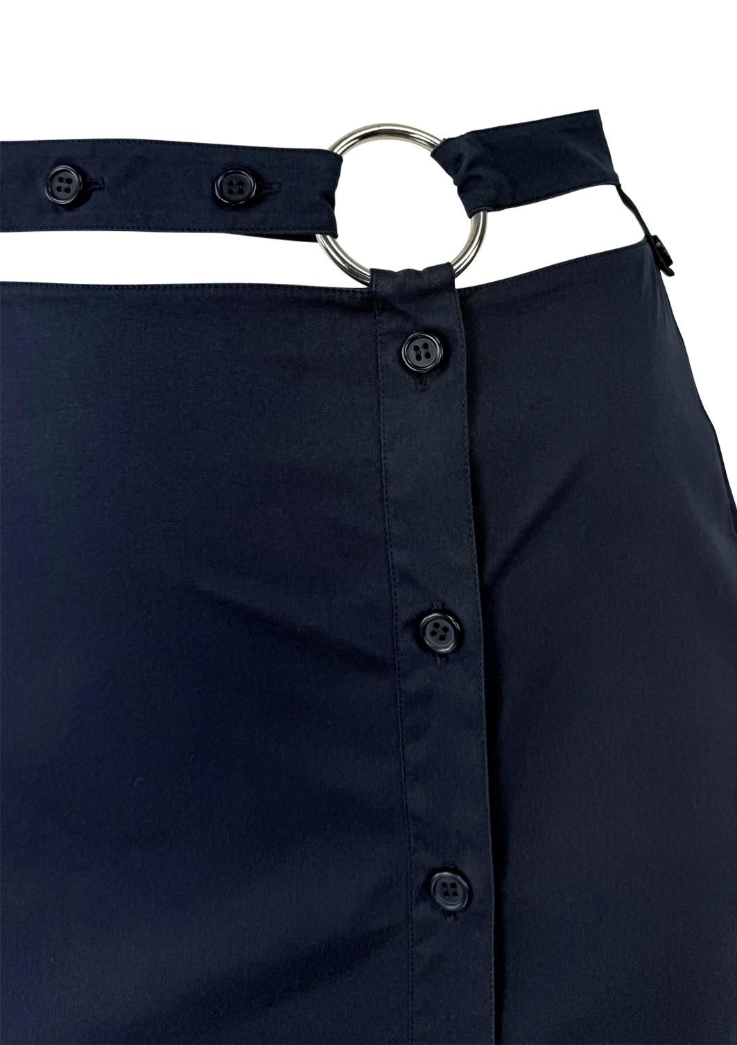 This 1990s Prada navy maxi skirt features a button-down front, a pleated flare hem, and a structured silhouette. The design is cinched at the waist with a contrasting chrome ring belt, adding a refined, utilitarian touch.

Approximate