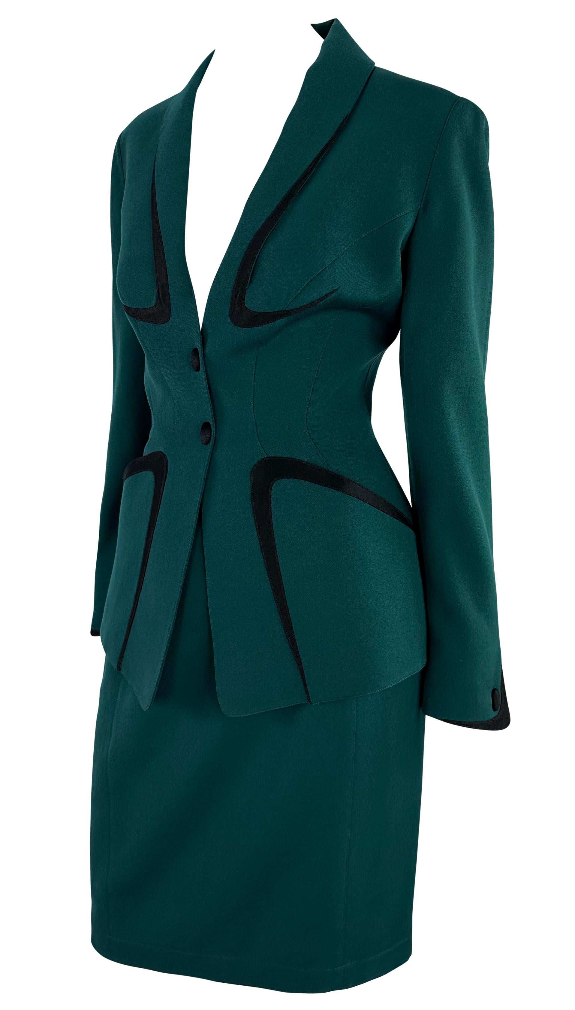 This incredible deep green Thierry Mugler skirt suit perfectly captures the structured and seductive style Manfred Mugler is known for. The striking suit features a plunging neckline and a tapered waist, highlighted by bold black velvet angular