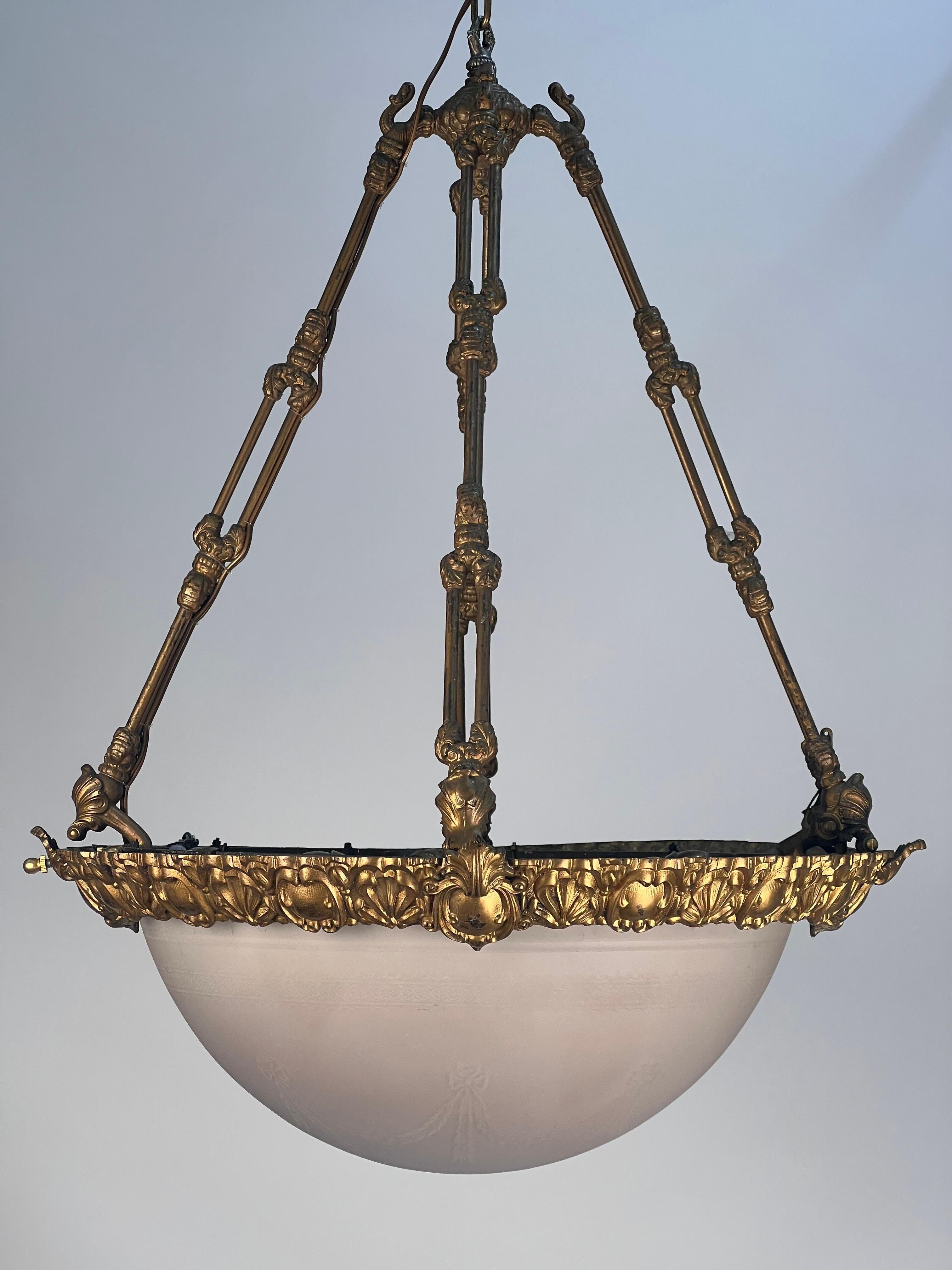 An exceptional late 19th century brass gas/electric pendant bowl. The pale ping acid etched glass bowl is original to the fixture. The etching of festoons with bows and bell flowers. Along the top parameter of the glass is a band of half circles