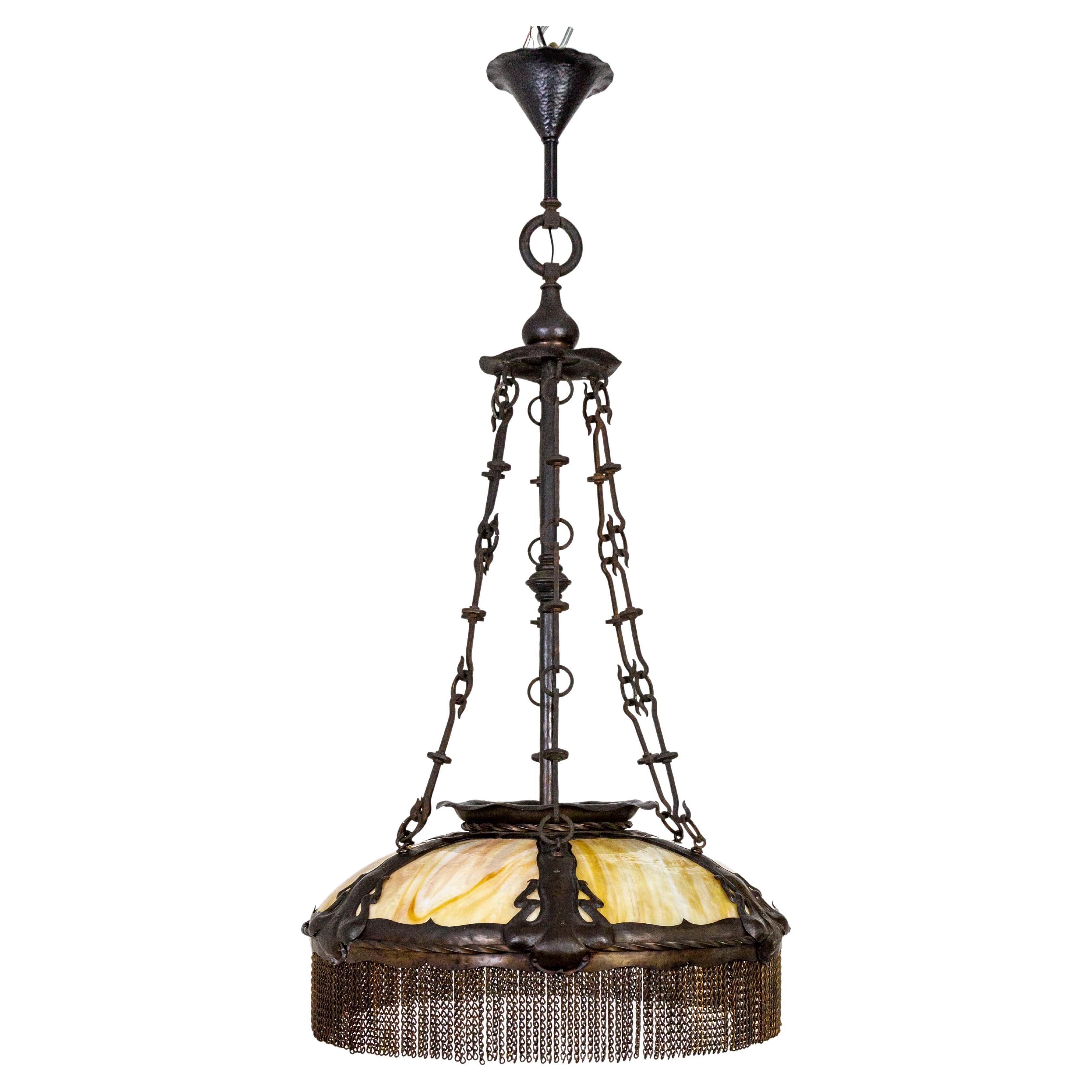 A large scale light fixture, originally gas, made circa 1878, with flowing Art Nouveau styling, hammered details, four hand-wrought, decorative chains and brass banding. Within the bronze and brass structure is parasol shaped, slag glass, in peach,