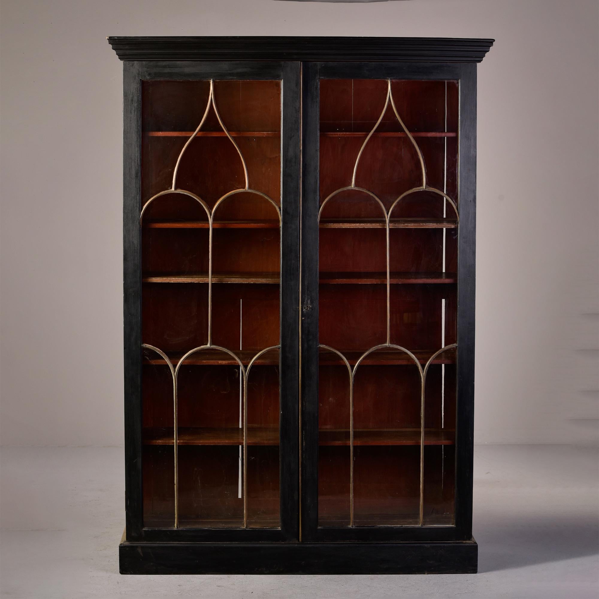 Circa 1890s tall English bookcase with gothic style brass glazing bars on front doors. Each side has five adjustable shelves. Functional lock with key on door. Exterior is painted in matte black and contrasts nicely with dark wood interior. Unknown