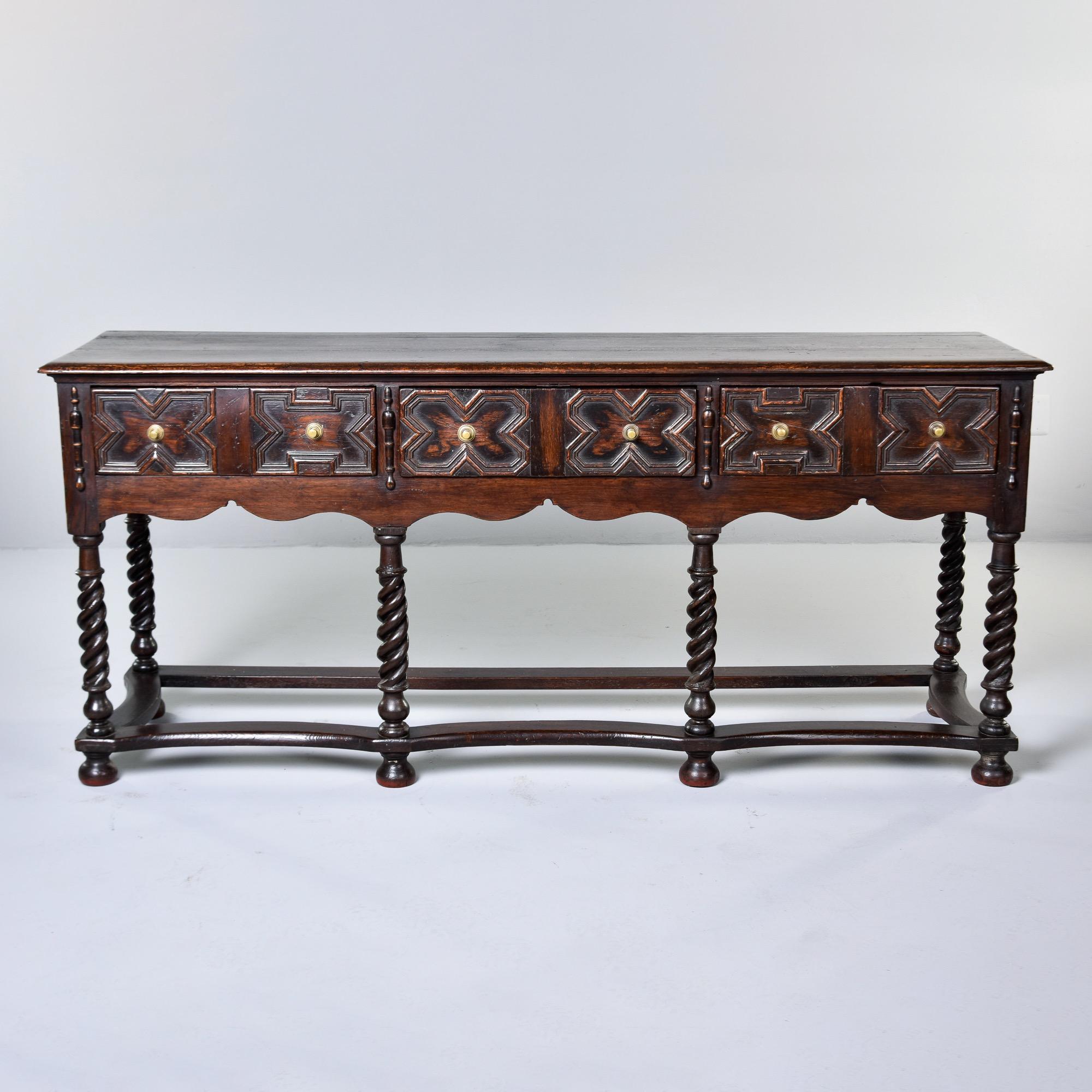 Found in England, this gothic style carved oak dresser base dates from the 1880s. Dark stained oak piece has eight hand carved, thickly twisted legs joined by stretchers at the base. Three functional drawers on the top with x-form carved details on