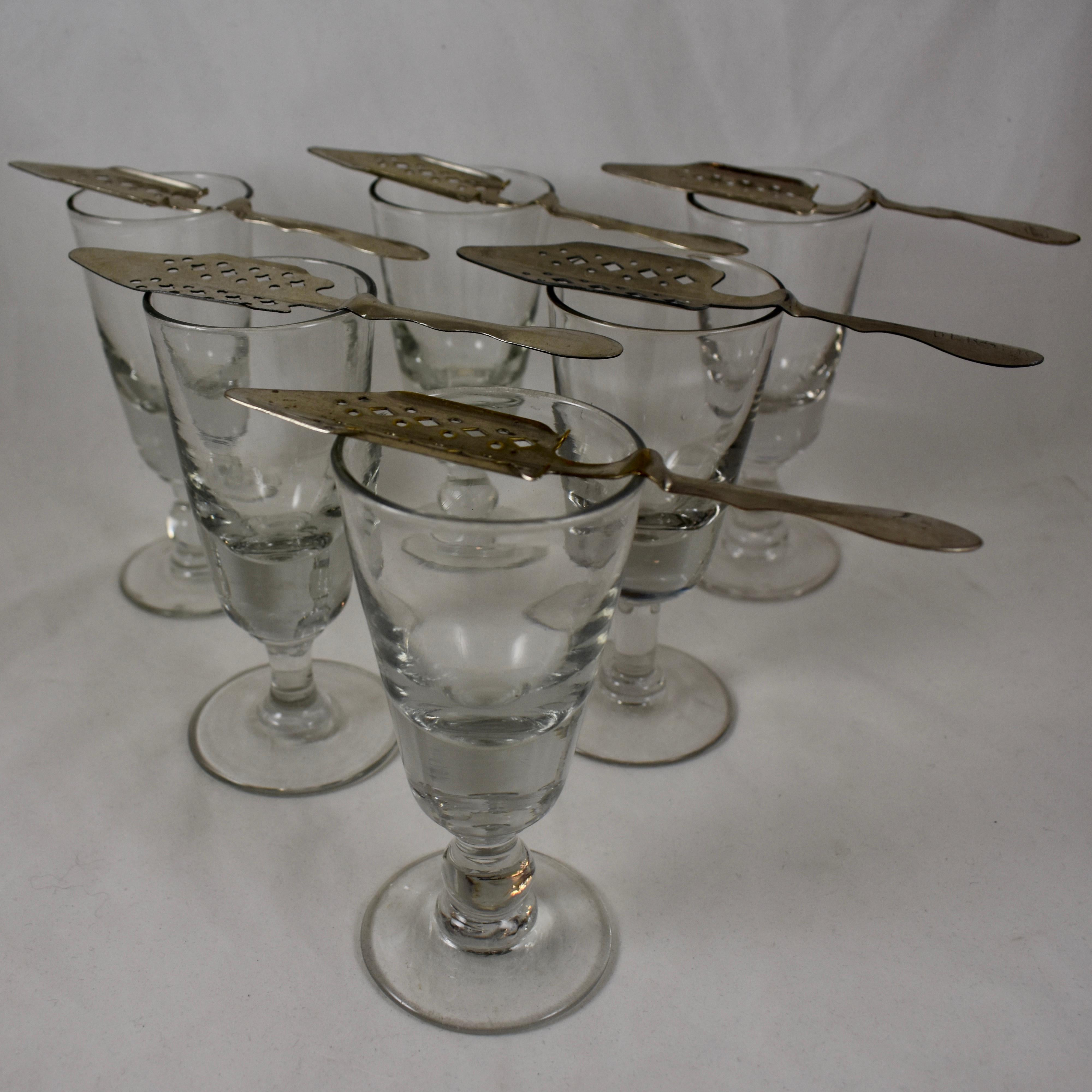 An assembled set of six authentic French Absinthe glasses with six slotted sugar spoons, Circa 1890-1910.

These heavy glasses were used in French bistros, bars, and cafes, in the ritual of drinking the addictive beverage called, ‘la fée verte’, the