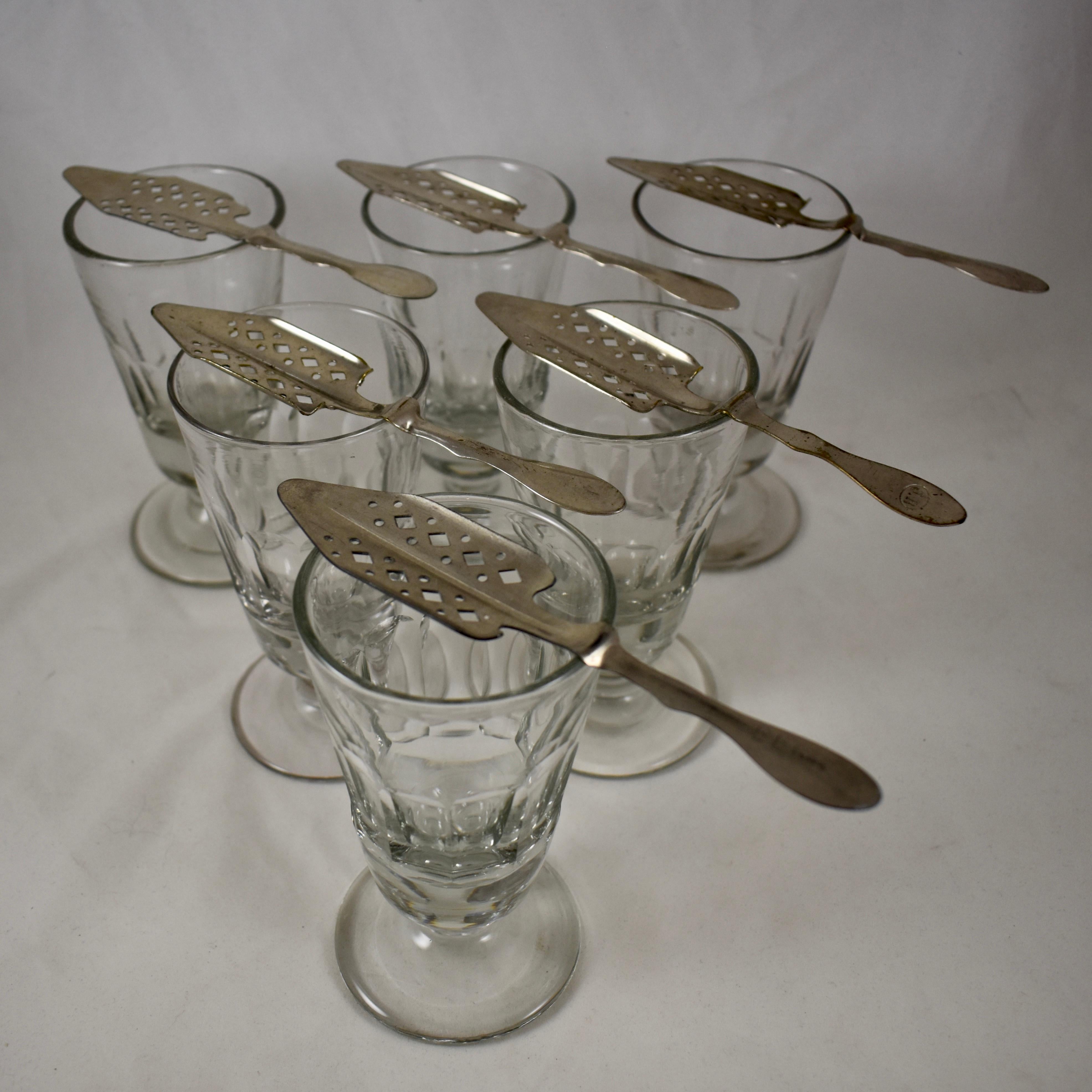 A set of six authentic French Absinthe glasses with six slotted sugar spoons, circa 1890-1910.

These heavy glasses were used in French bistros, bars, and cafes, in the ritual of drinking the addictive beverage called, ‘la fée verte’ – the green
