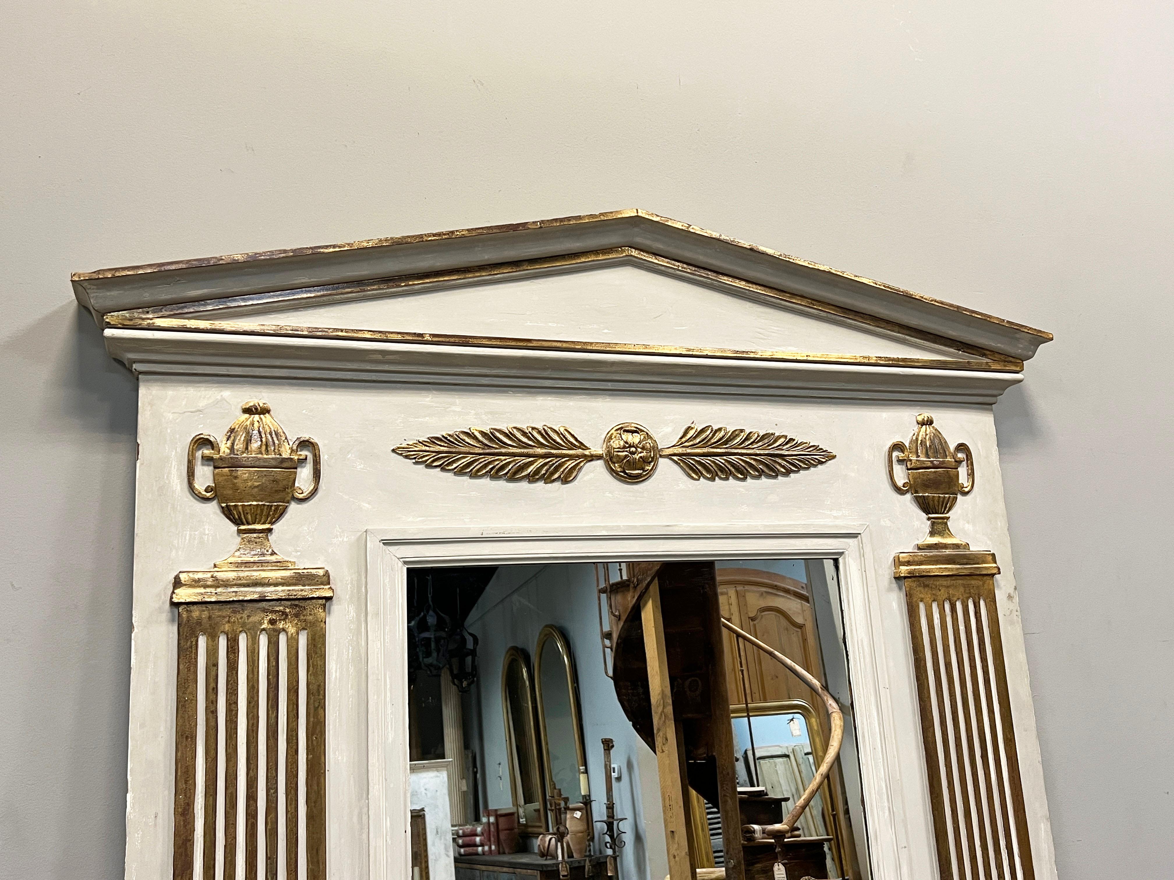 This is an impressive classically styled yet restrained overmantel mirror and frame, painted with gilded decorative elements. Fluted pilasters are topped with a classical urn with pediment echoing the classical Empire style.

Mirror frame likely