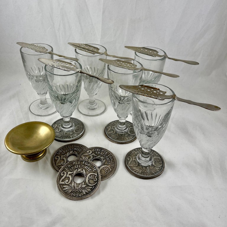 Everything needed to prepare and serve the distilled spirit Absinthe – a set of six French Absinthe glasses, six slotted sugar spoons, six metal drink coasters, and the sugar stand. The glasses, spoons, and the stand de sucre date from 1890 to 1910.