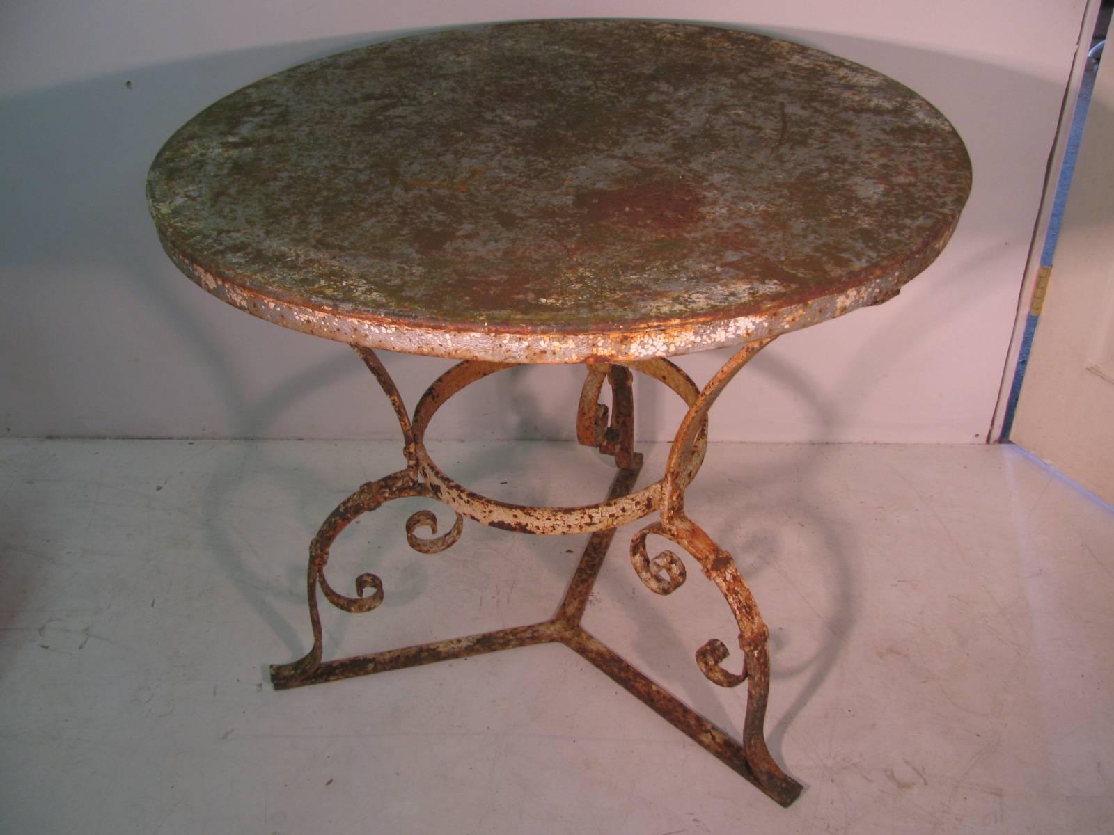 Fabulous round garden table suitable indoors or out. Heavy wrought iron base with scroll work on tripod. Heavy sheet metal top with all the original patina, some paint some rust. Hand riveted together. Top has been lightly sanded to remove any loose