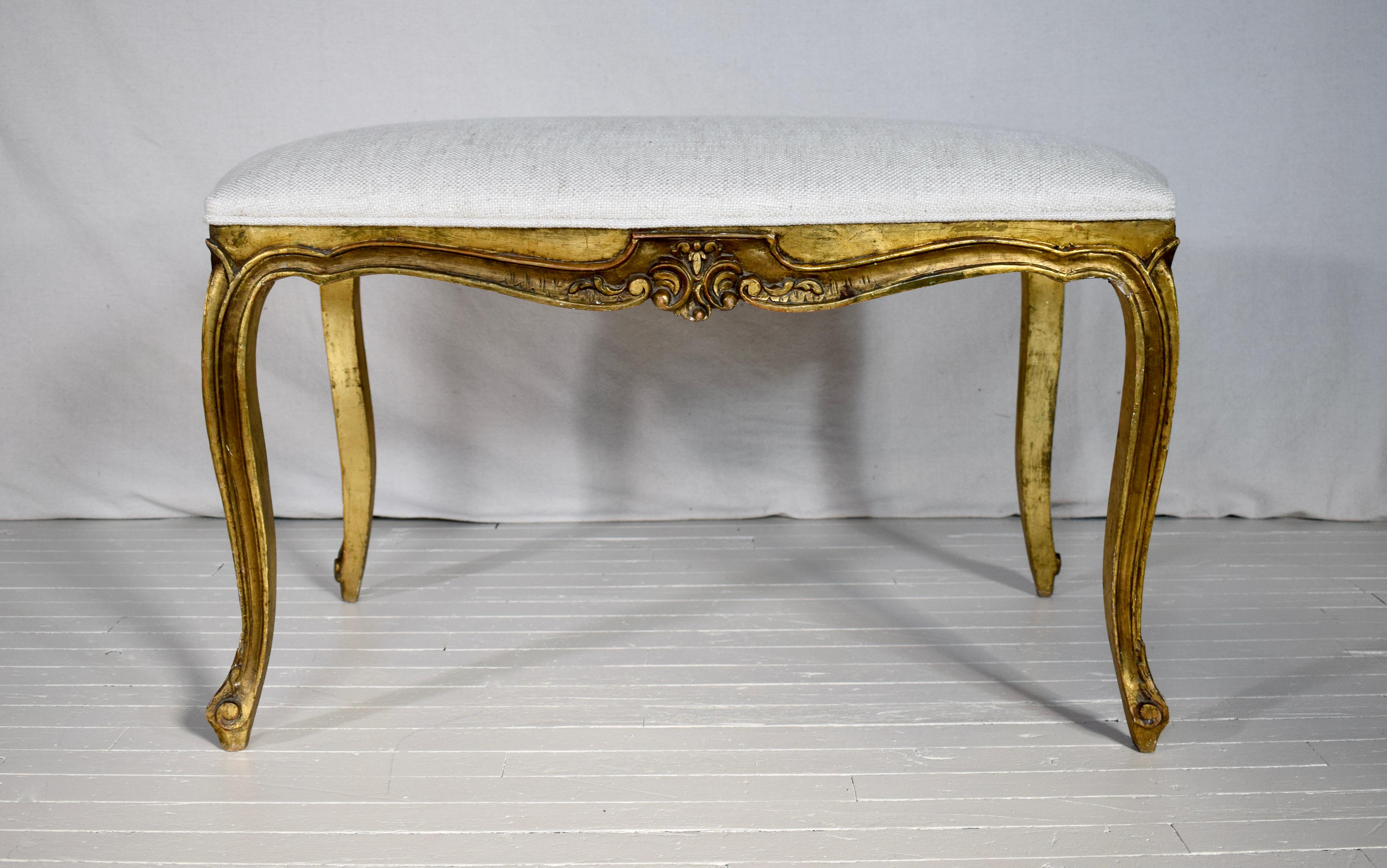 Late 19th early 20th c. French Louis XV Style Giltwood bench with intricate hand carvings & warm patina to the all original gold leaf gilt finish. Features new antique white woven cotton upholstery.