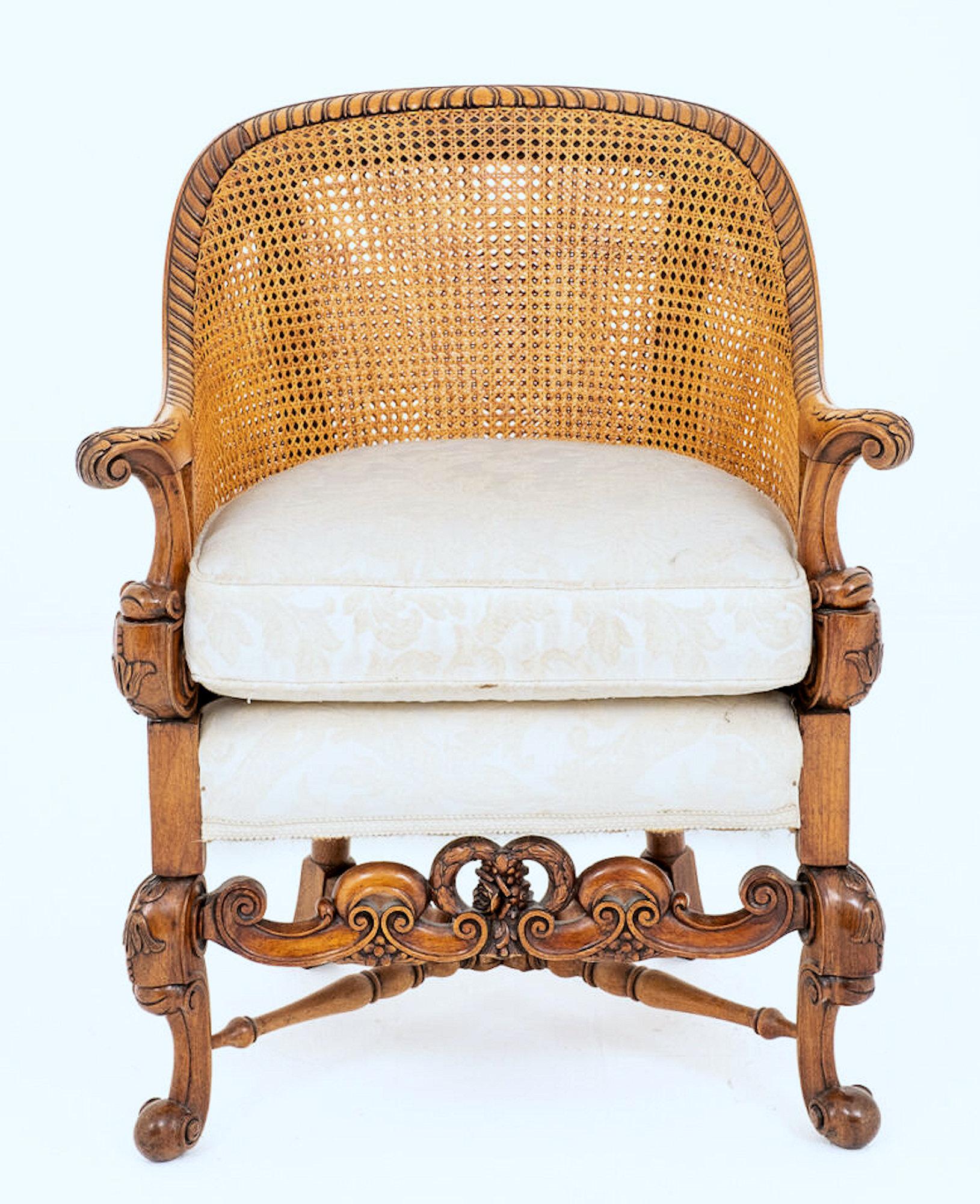 This beautiful and ornately designed 19th century mahogany bergère chair in the Carolean style features squat cabriole carved legs and an elaborated carved front stretcher bar. The arm supports are nicely carved with acanthus leaves and there is an