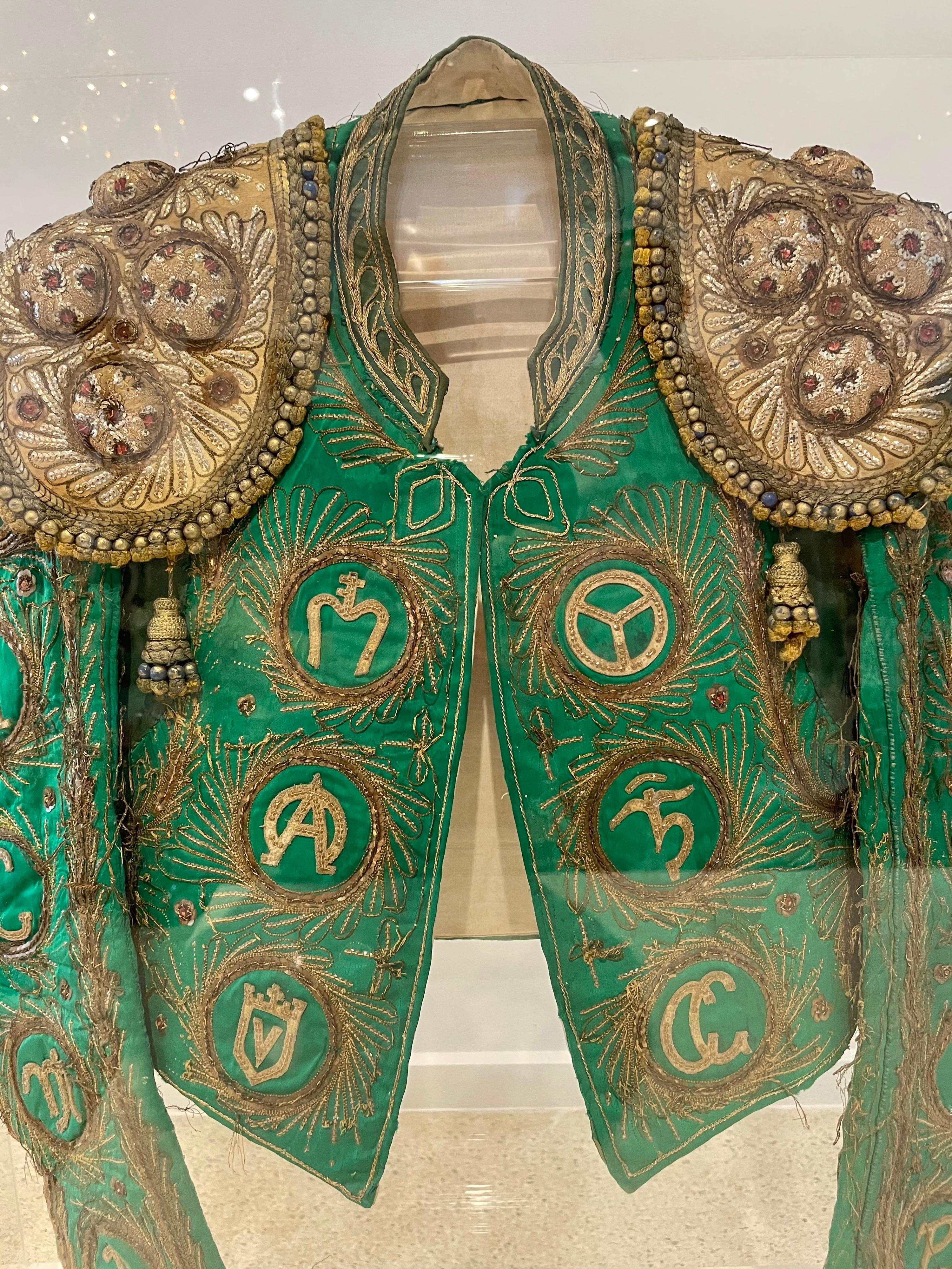Encased in a magnificent acrylic display box, this very luxe, rare, antique embellished bull fighter's jacket (Traje de Toreador) with detailed embroidery and separate epaulettes. 

This vibrant green Toreador jacket is a unique piece which is