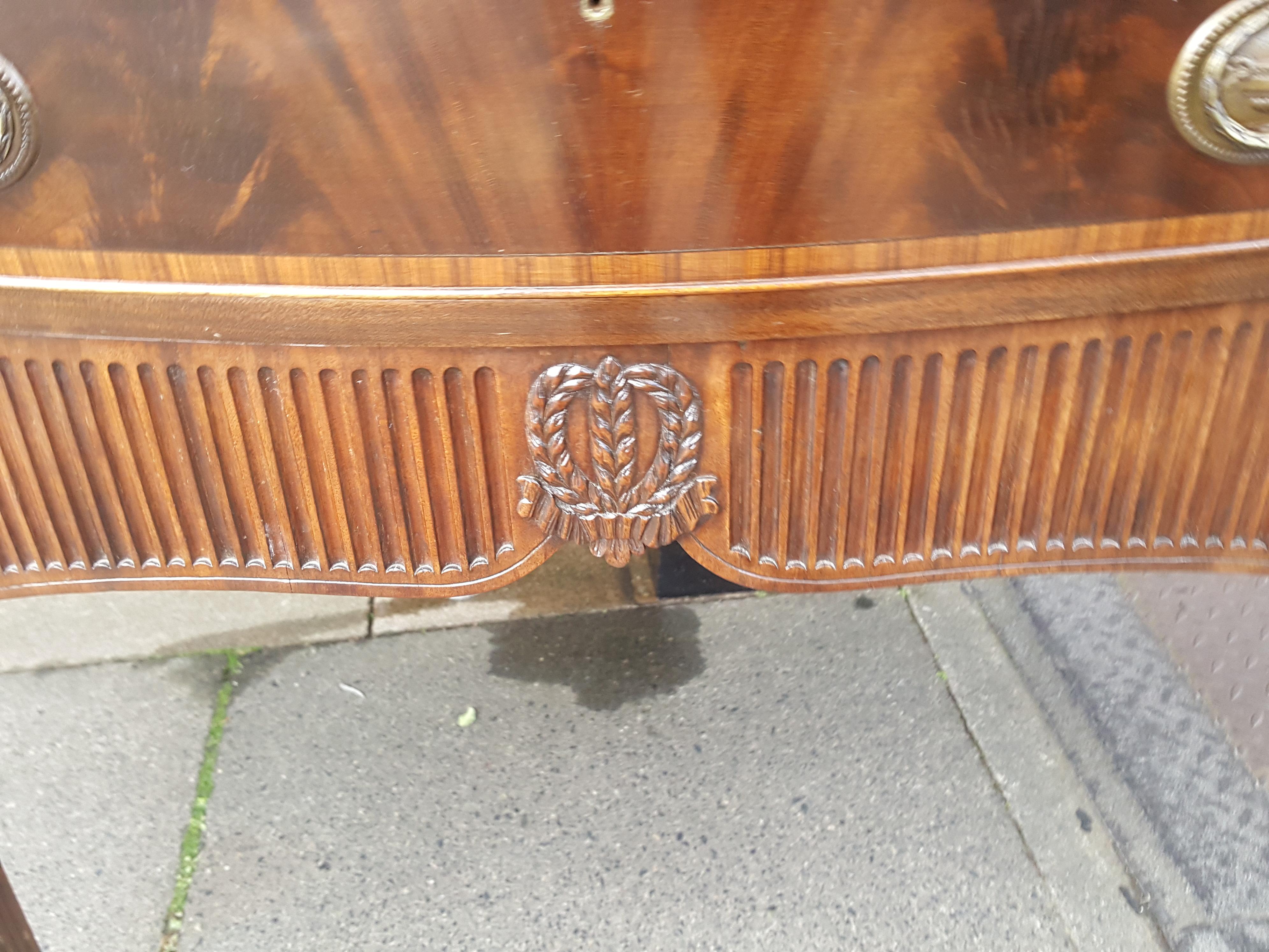 A late 19th century Adams style mahogany and rosewood sideboard, with serpentine front having a kingwood crossbanded edge above a series of drawers and cupboards with brass drop handles, flanked by wheat and foliate carved pilasters, with fluted
