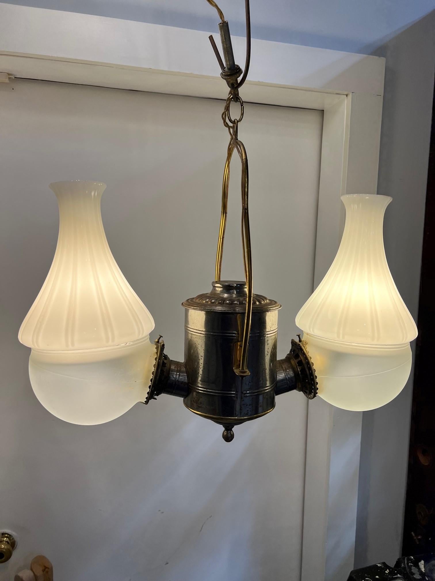 This is a 1890s double light hanging fixture by Angle Lamp Company. Originally lit by kerosene it has now been electrified. It has the original glass pieces two frosted, hemisphere globes that are topped with white chimney milk glass with scalloped
