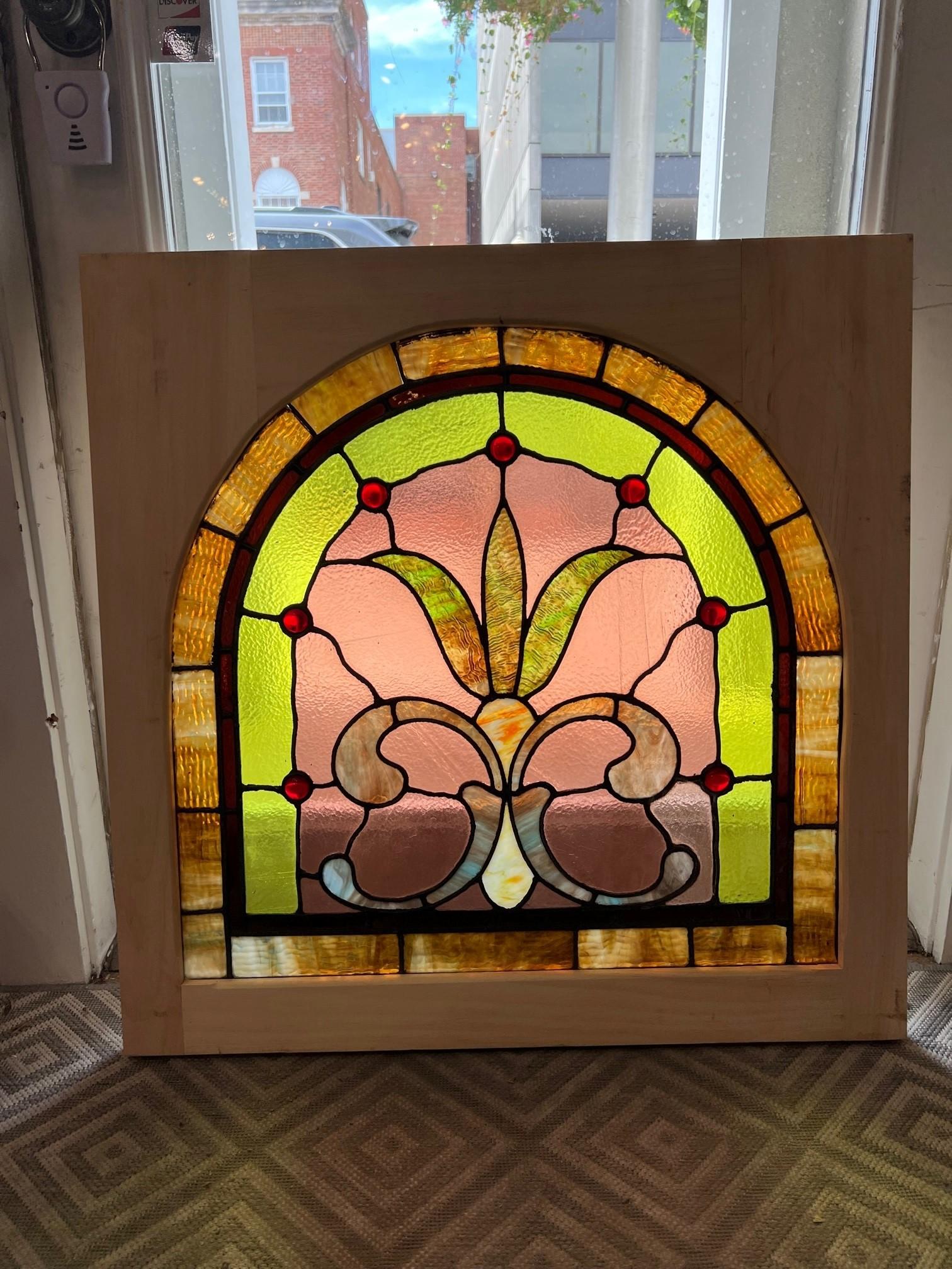 Beautiful antique arched stained glass window with jewels and good colors. This antique stained glass window was salvaged from an estate outside Pittsburgh PA. It has been put into a new wood frame making it easier to hang and install. With the arch