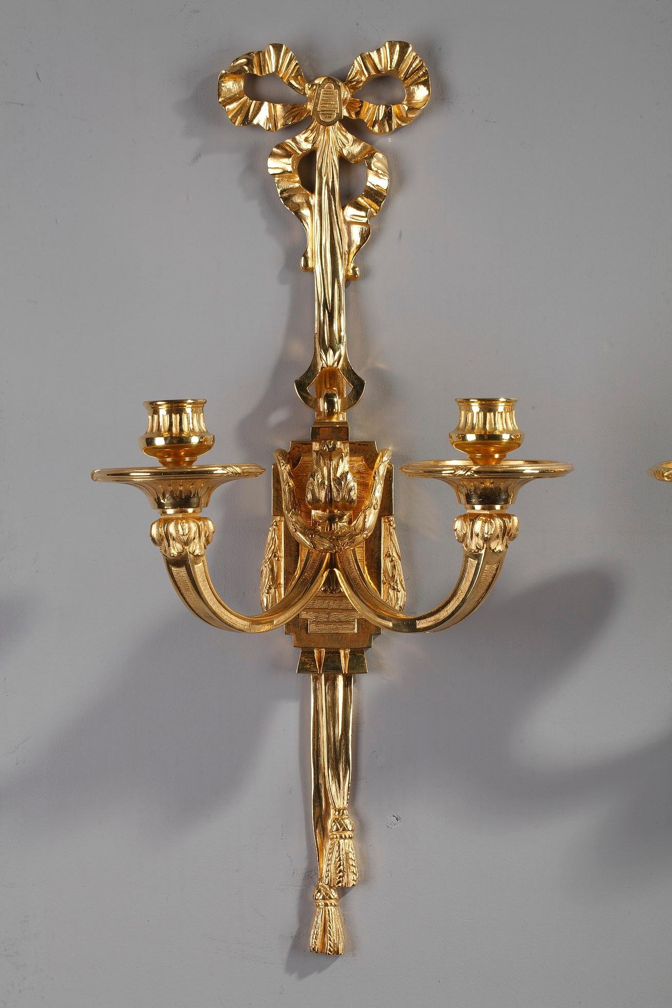 A pair of French late 19th century Louis XVI style antique candle wall sconces crafted entirely of gilded bronze with two lights decorated with acanthus leaves. The fluted stem highlighted with foliage, laurel garlands and two hanging tassels in the