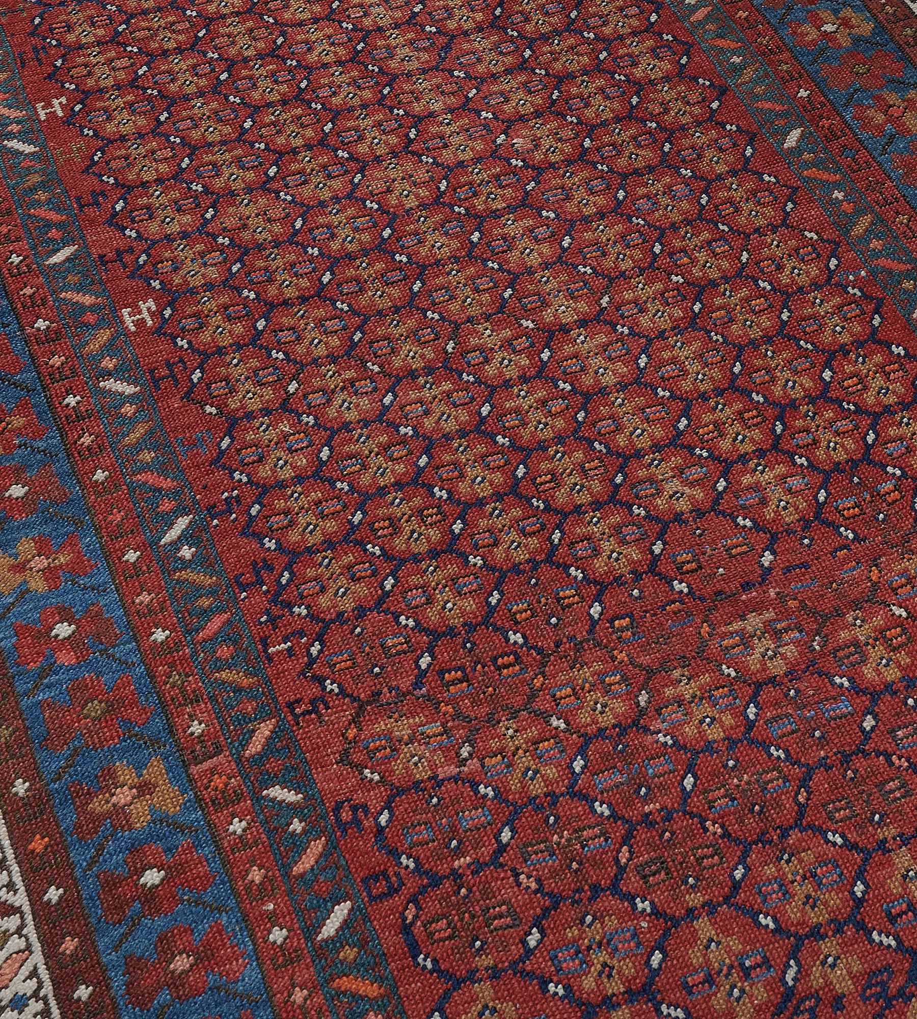 This antique rug has a tomato-red field with an overall design of linked indigo-blue lozenges, each containing a pair of polychrome square lozenges around a central sandy-brown angular floral stem, stylized animals at each side, in a light blue