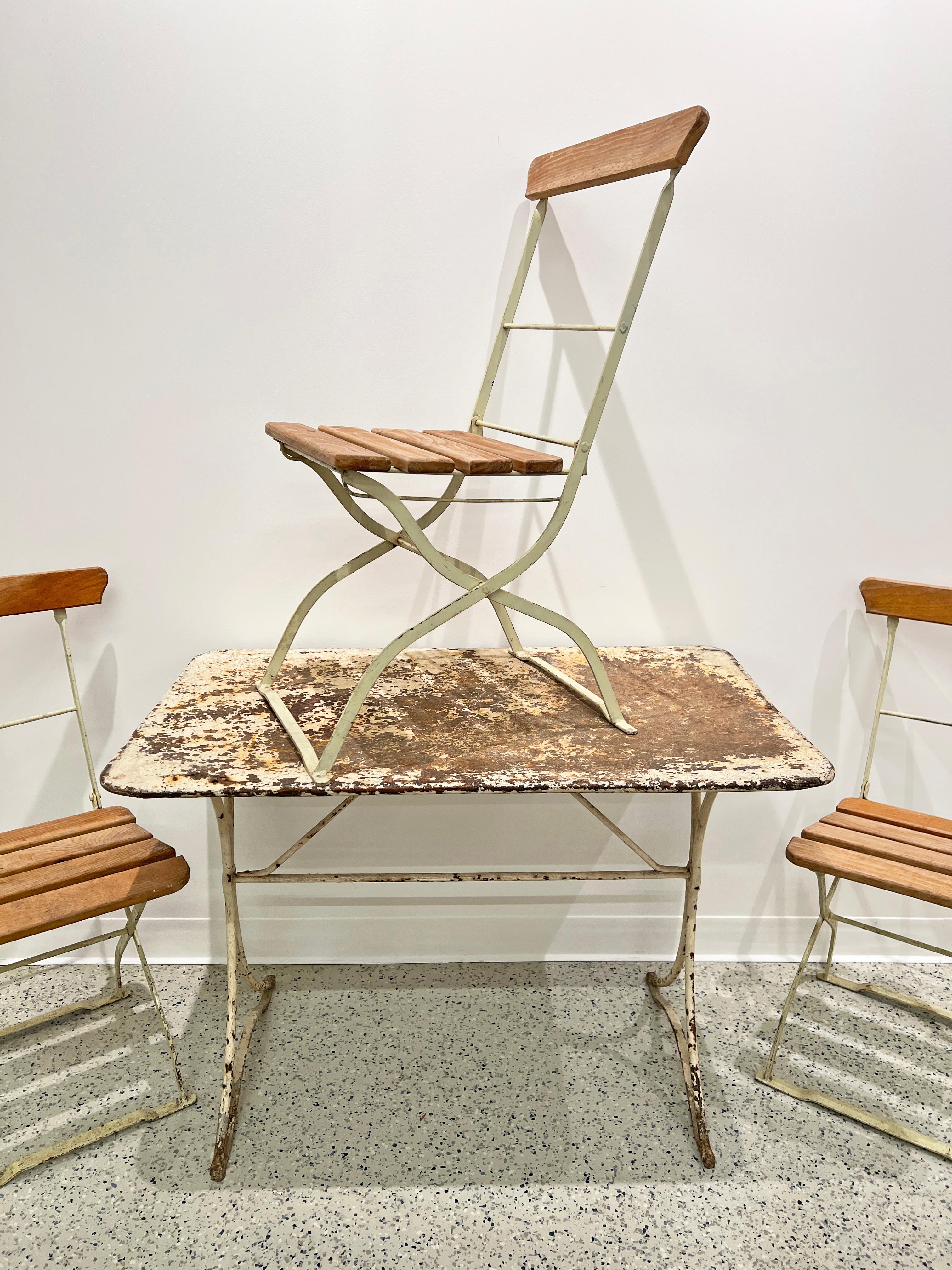 A late 19th century antique French cafe set of three “Simplex” folding chairs and steel bistro table in original distressed finish, chair slats have been professionally replaced and varnished. Folding furniture became immensely popular with