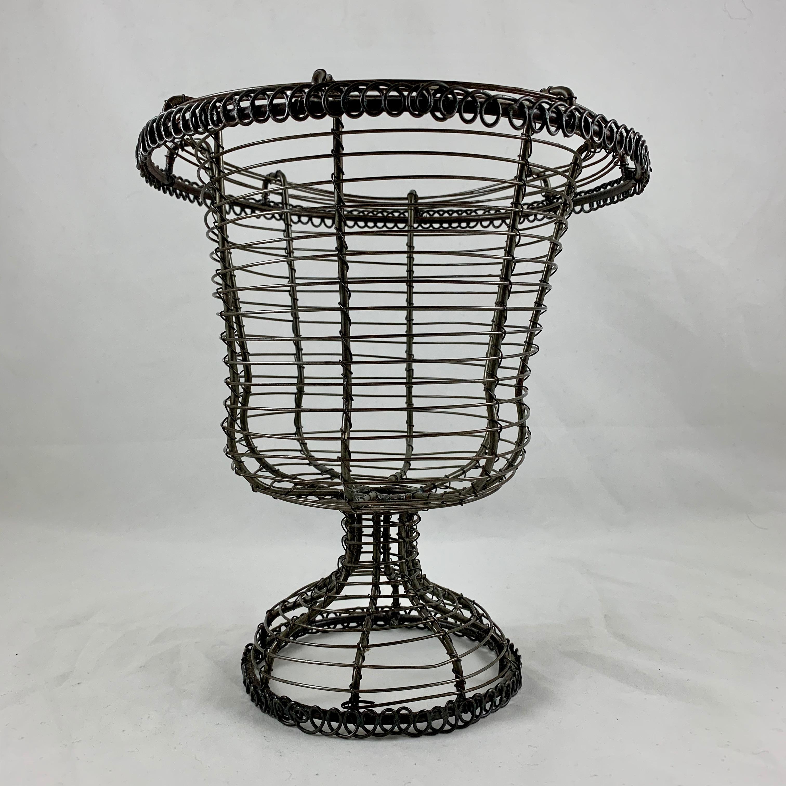 From France, circa 1890-1910, a pedestal base, urn form twisted wire standing basket with an upper rolled rim.

Amazing as a table-center or on a kitchen countertop, used as originally intended throughout Provençal France for holding fresh eggs,