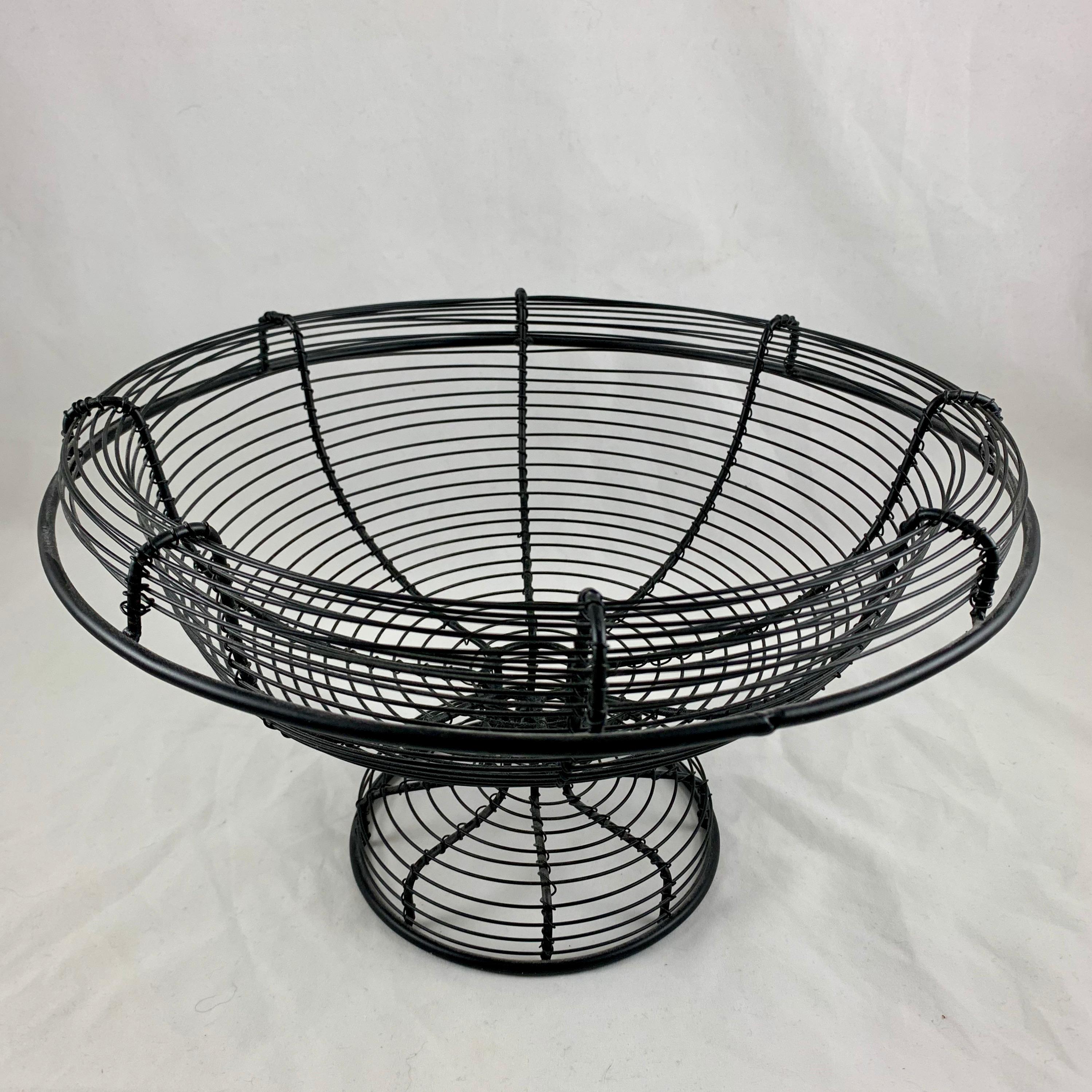 From France, circa 1890-1910, a pedestal base, urn form twisted wire standing basket with a wide upper rolled rim.

Amazing as a table-center or on a kitchen countertop, used as originally intended throughout Provençal France for holding fresh