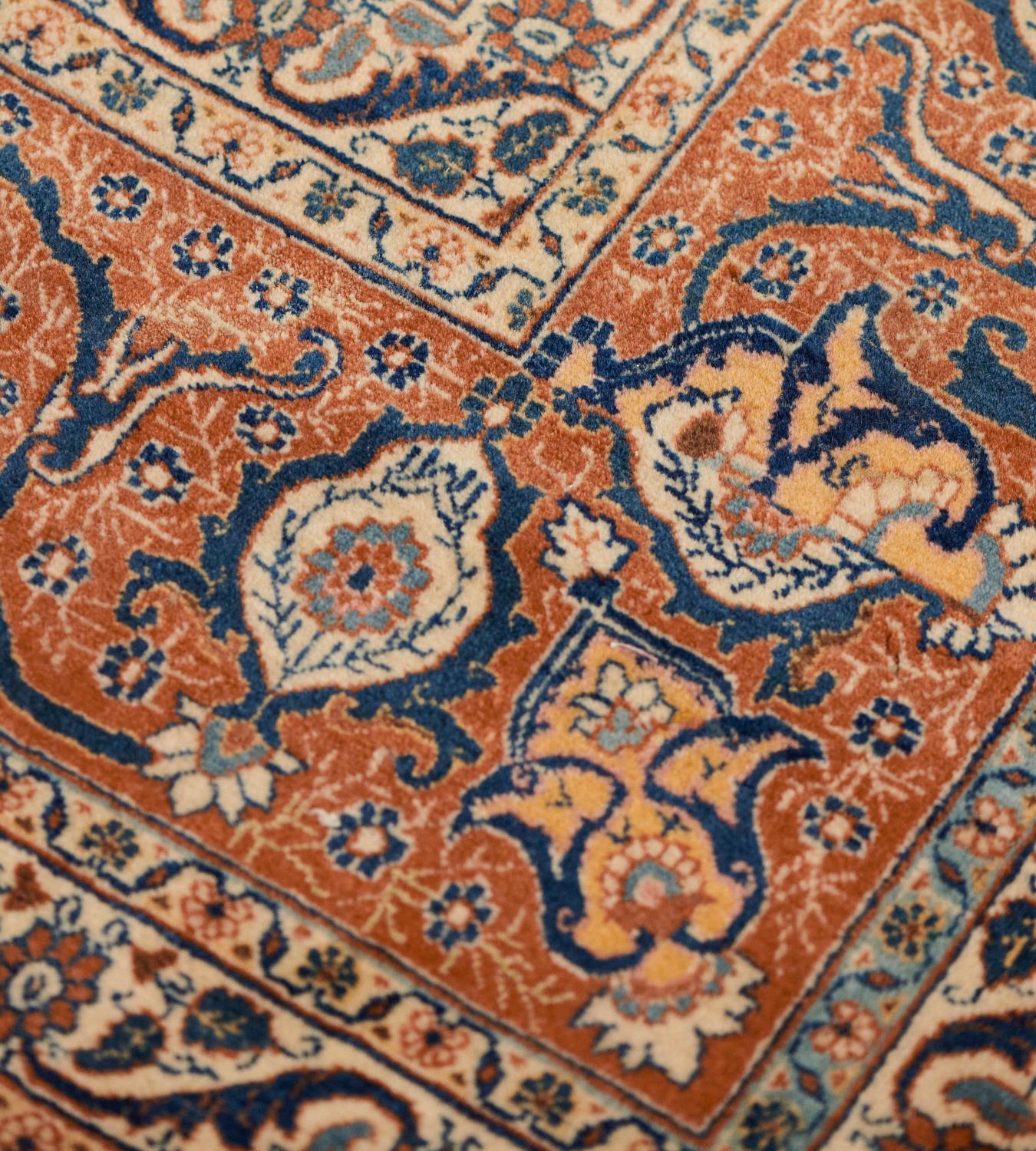 This antique Hadji Jallili rug has a shaded royal-blue field with an angular apricot and brick-red arabesque vine linking bold stylized trees and plants surrounded by delicate shaded green leafy plants and a dense profusion of floral sprays and