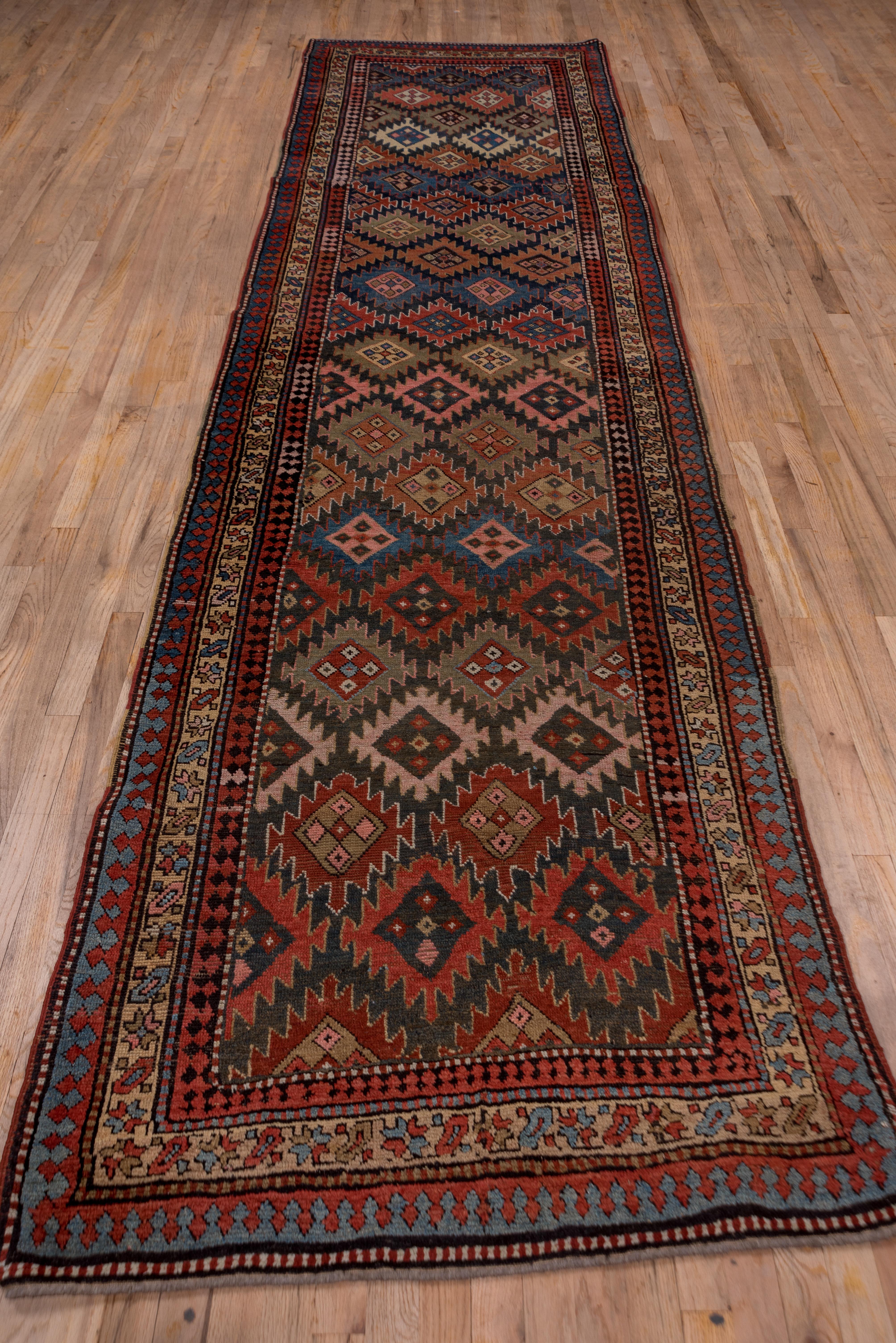 The bottle green ground displays colorful medallions in red, mustard, blue, coral and pale green. This medium coarse southern Caucasian runner has a central ivory star and diagonal border between reciprocal keyhole guards. A generally attractive