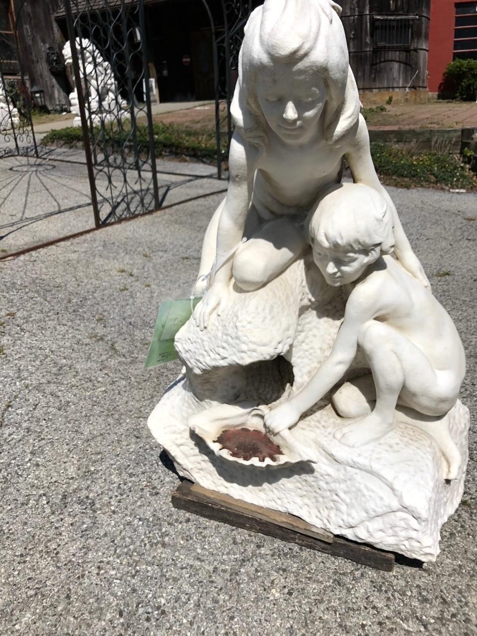 Marmorbrunnen aus dem frühen 20. Jahrhundert mit einem Mädchen und einem Jungen, die eine Muschel halten, während das Wasser aus den Felsen kommt. Während der Junge die Muschel hält, schaut das Mädchen hinüber, während das Wasser fließt. Es ist ein