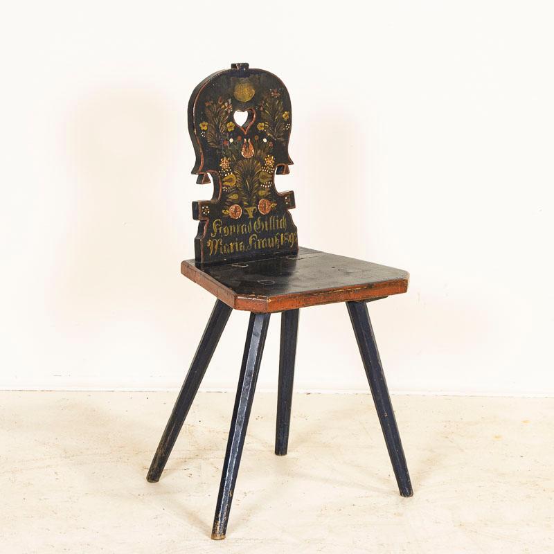 This delightful peg leg chair has a traditional heart shaped cut-out in the back, which brings to mind a quaint cottage in the European countryside. The original dark blue paint is accented by red, yellow and green folk art stencil/painted flowers