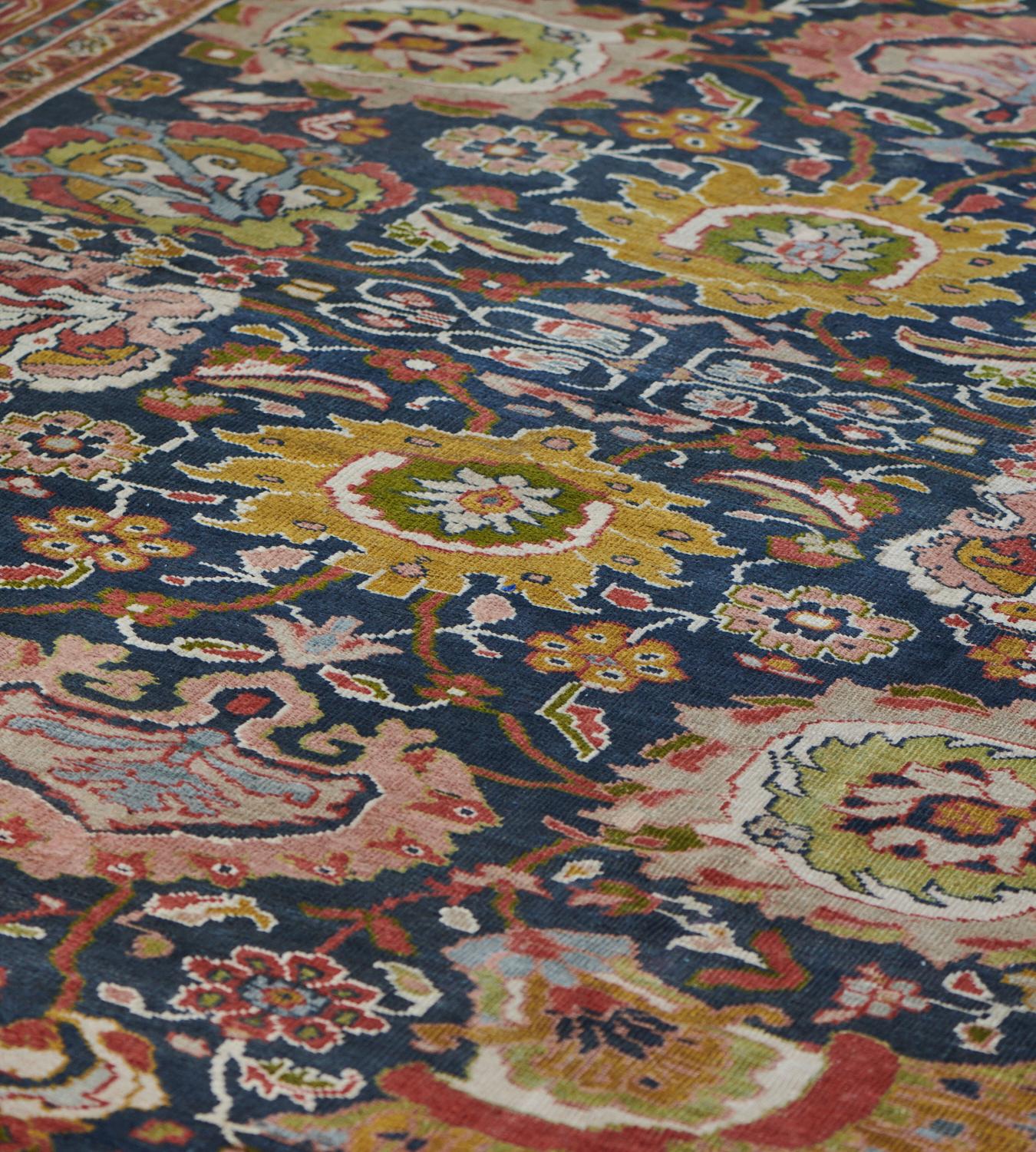 This antique Ziegler carpet has a shaded royal-blue field with an overall design of bold polychrome palmettes around a central column of similar palmettes all linked by a scrolling floral and leafy vine, in a brick-red border of lime-green and