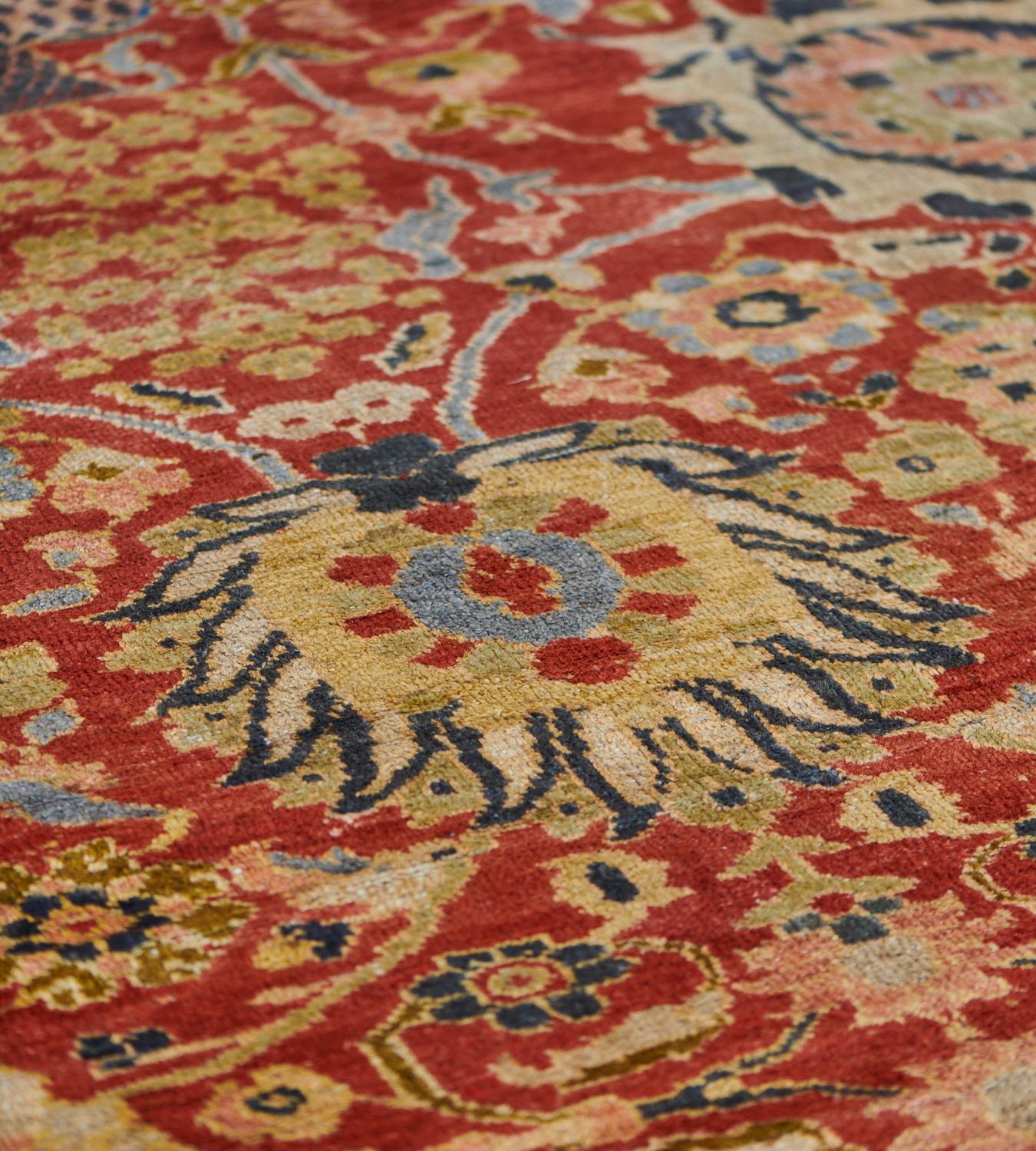 This antique Ziegler Sultanabad rug has a red field with a flowering vase and bold palmettes at each end with vertical rows at each side of bold polychrome palmettes linked by dense polychrome floral and leafy vine, in a broad indigo-blue border of
