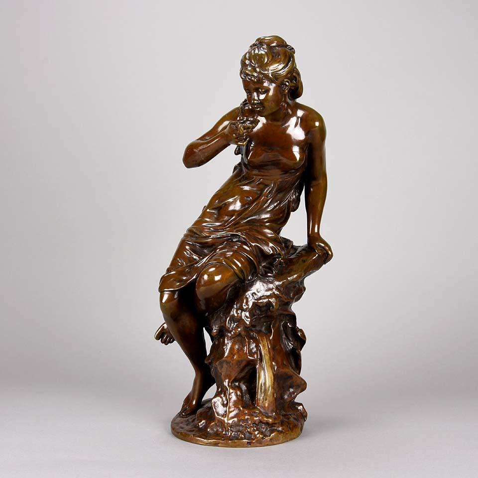 A charming late 19th Century bronze study of an Art Nouveau beauty seated upon a tree stump dressed in loosely fitted attire drinking from a shell. The surface of the figurine with excellent hand finished detail and rich colour, signed Math