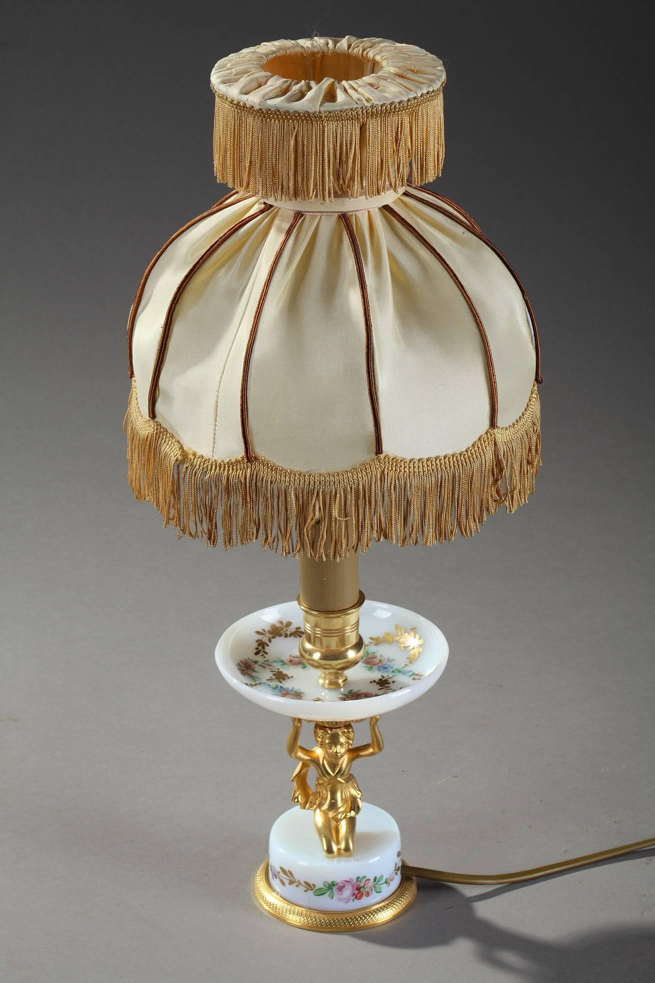 19th century table lamp featuring a gilt bronze putto knelt down on a small opaline base decorated with polychromatic flowers. He is holding an opaline cup above his head in his upraised arms. The cup is highlighted with polychromatic and gold