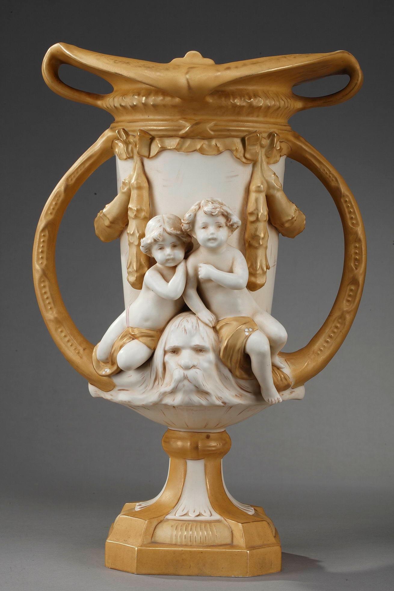 Royal Dux Bohemia vases beautifully crafted in white and gold-colored?porcelain, featuring children and bearded masks. Displaying a rich decor of ribbon and aquatic plant motifs, these vases exemplifie the style and decoration of the 1900 era.