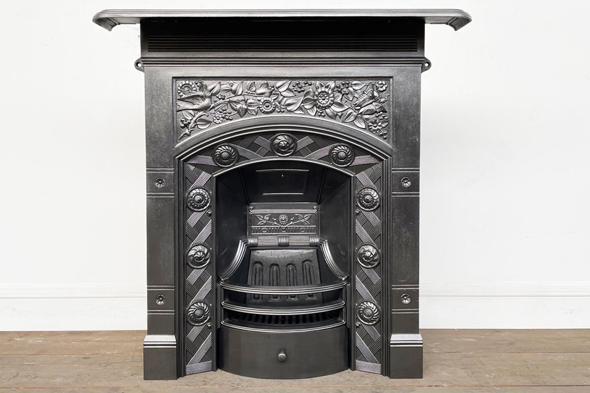 A beautiful late 19th century Arts & Craft cast iron bedroom fireplace. To the frieze, a songbird and butterfly are perched amongst branches bearing berries. Framing the slow arched aperture is basket weave design interspersed with decorative discs.