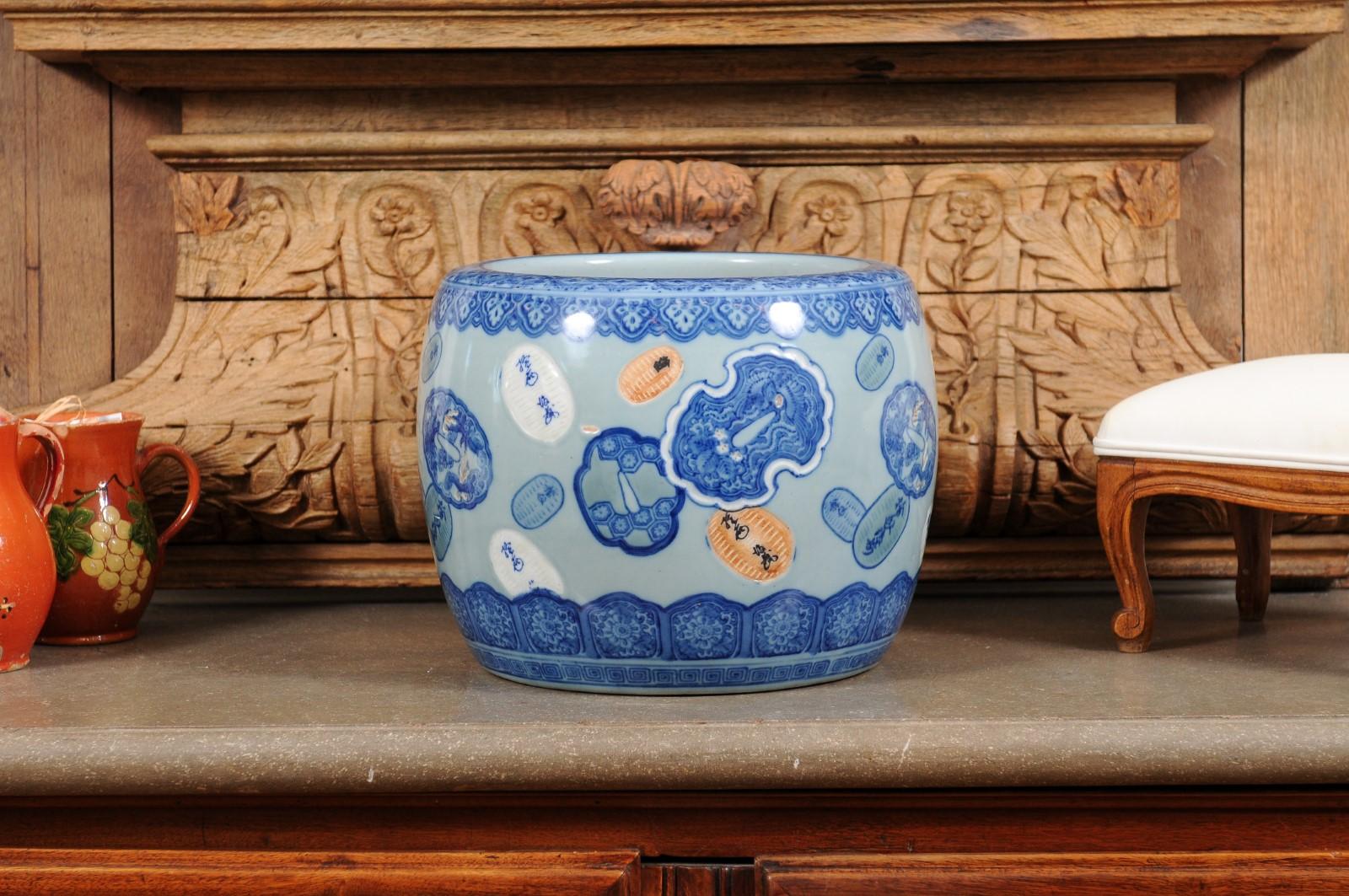 An Asian porcelain cachepot from the late 19th century, with floating cartouches and blue, white and orange tones. Created in Asia during the later years of the 19th century, this small cachepot charms us with its simple circular lines adorned with
