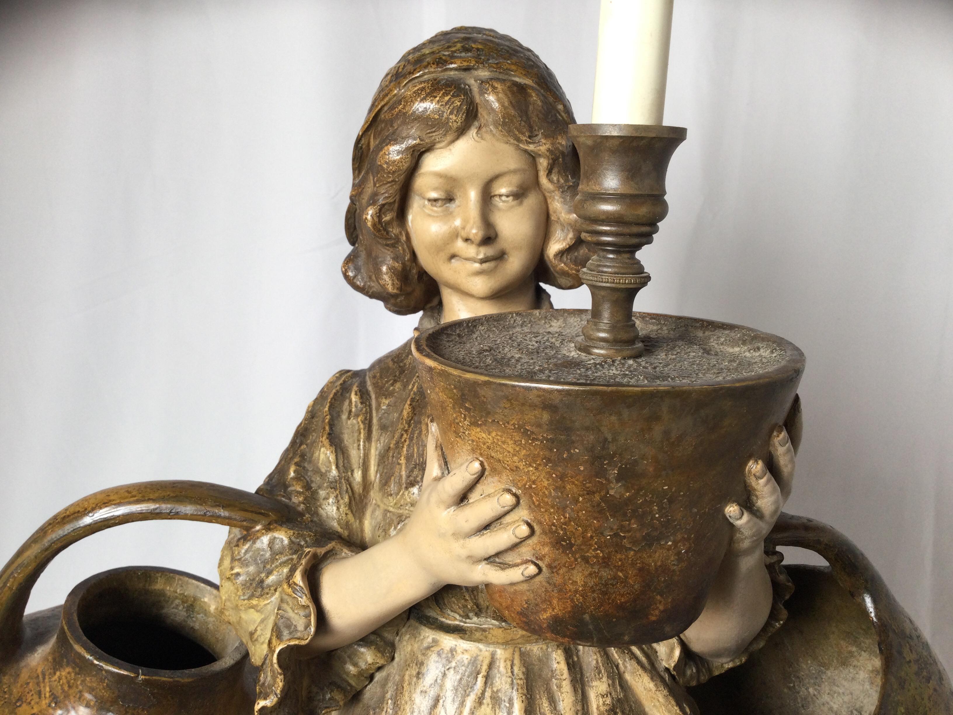 A 19th century Goldscheider peasant girl statue of polychromed terracotta. The figure with three jugs with the top fitted with a electrified candlestick. The makers mark are on the bottom.