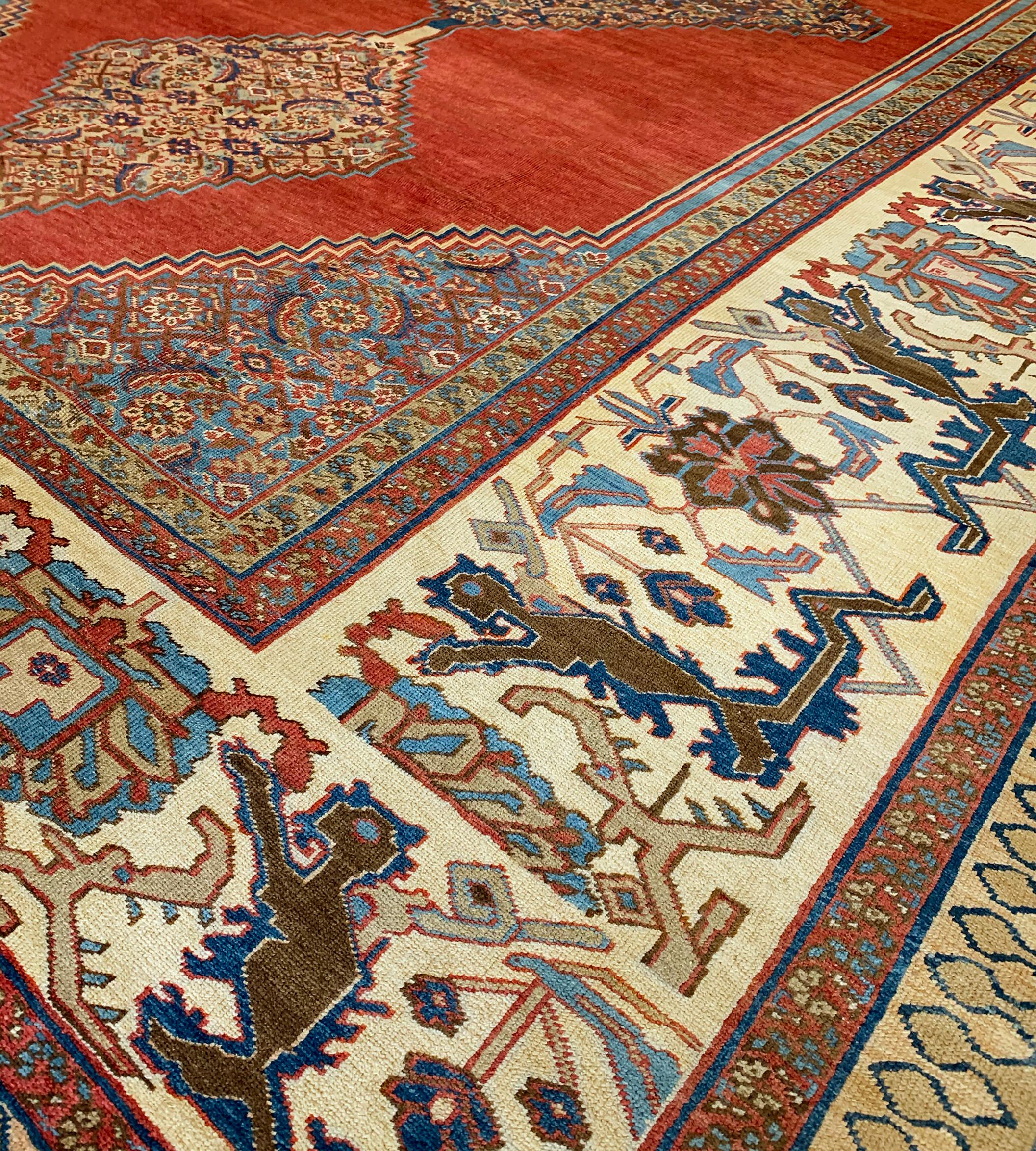 This traditional handwoven Persian Bakhshaish rug has a ruby field enclosing triple stepped lozenge Herati medallion, in similar shaded blue spandrels, with a broad ivory angled palmette vine border, between floral vine stripes, plain outer skittle