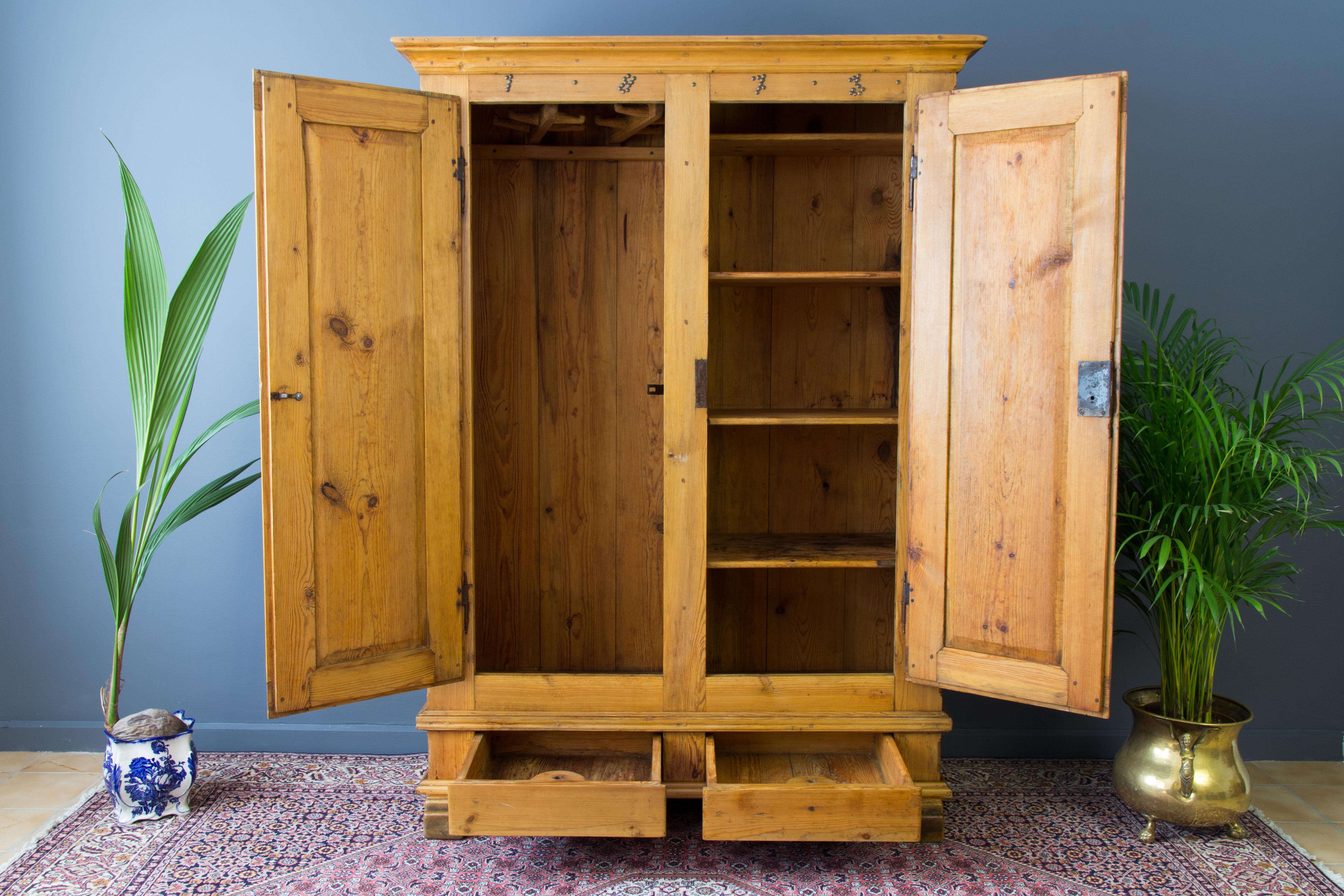 Made in excellent quality solid Baltic pine, with a pair of paneled doors and pair of drawers to the base. The inside of the armoire is divided into two parts. One side is equipped with four shelves, the other - with original clothes hangers, which